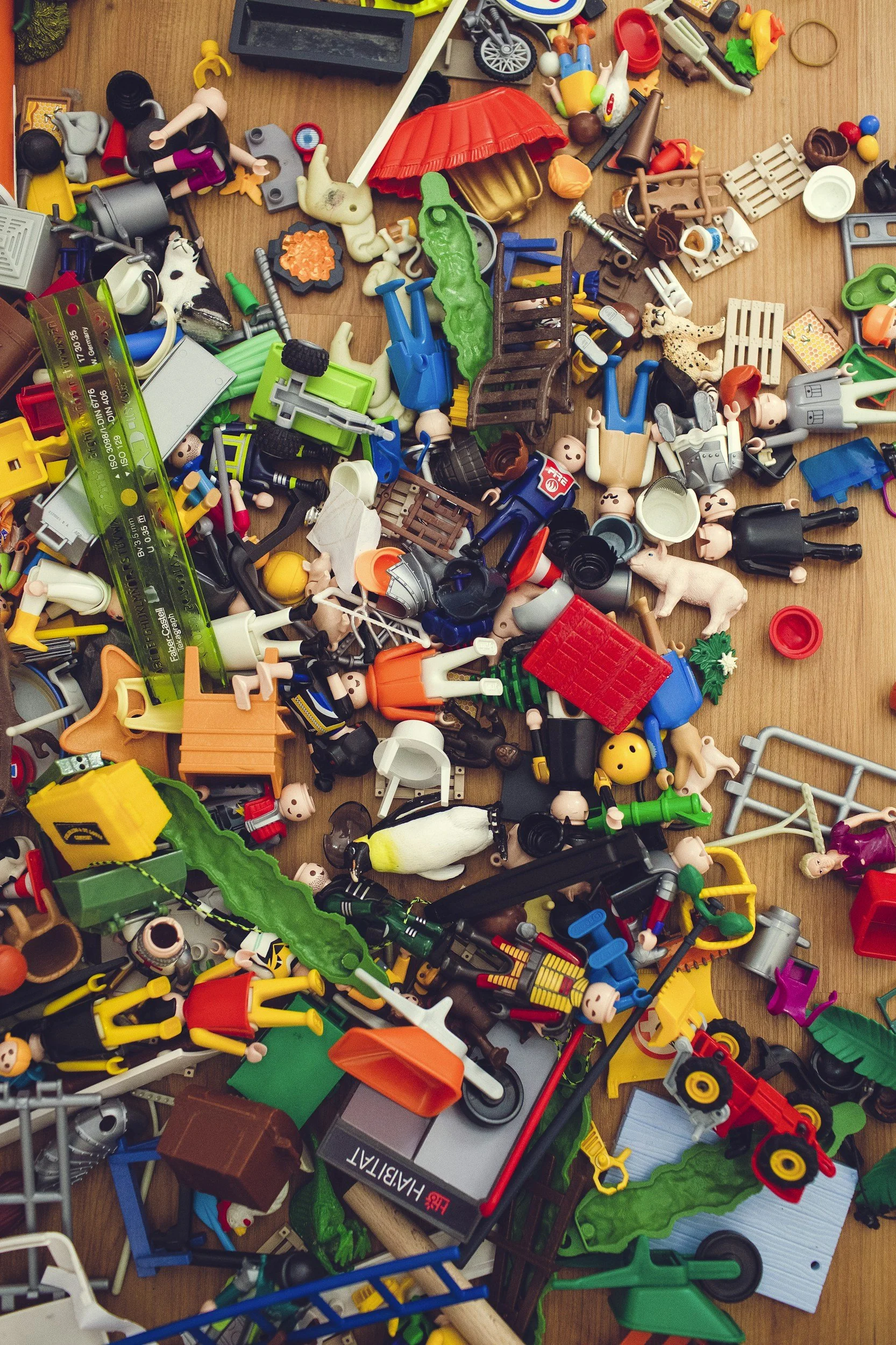 Eine bunte Ansammlung von Spielzeugteilen, darunter Figuren, Fahrzeuge und Zubehör, verstreut auf einer Holztischfläche.