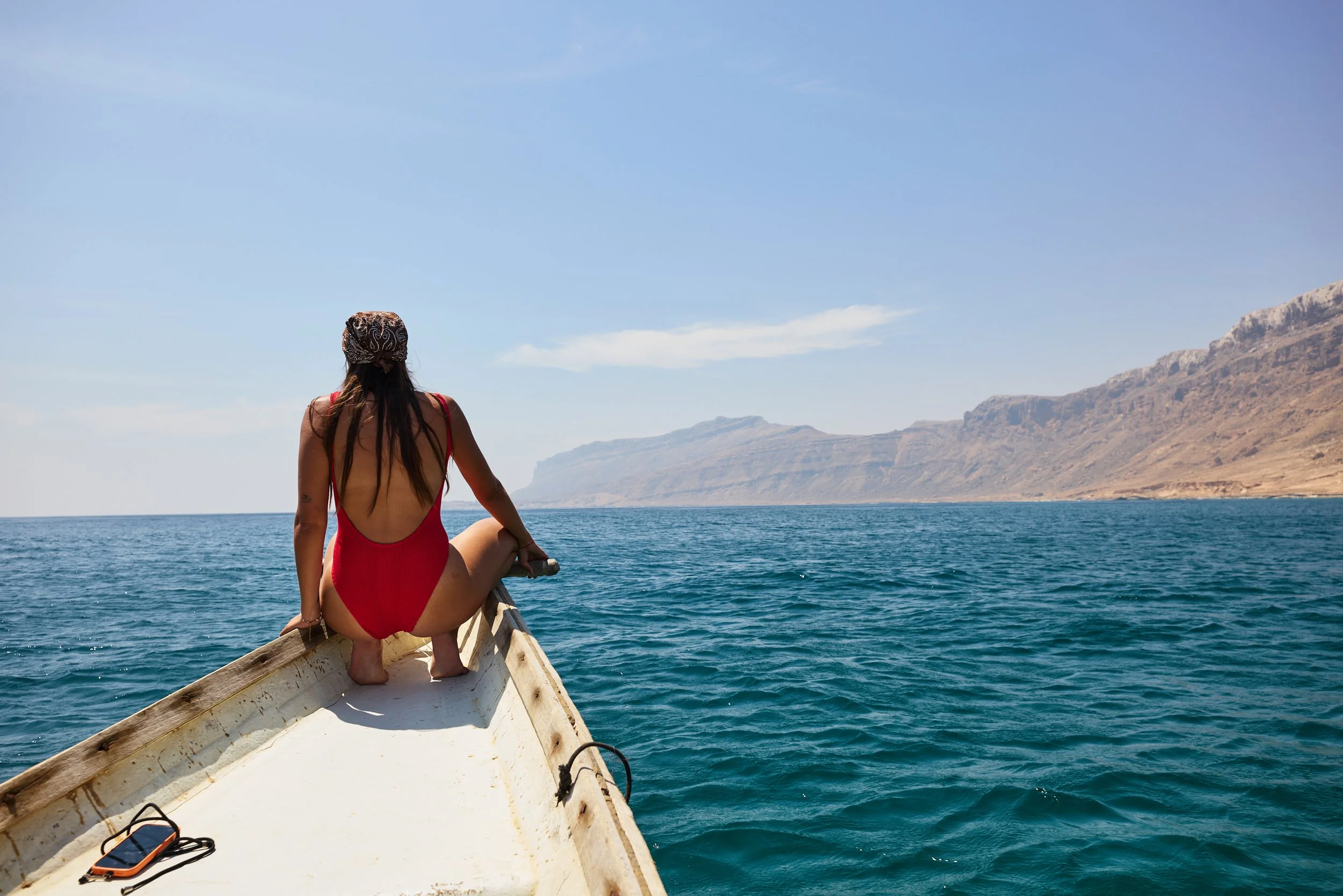 a girl in a red swimsuit sitting on the edge of a boat that is in the arabian sea off the coast of socotra