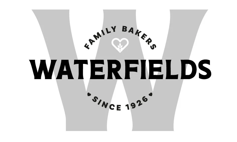 Black and white logo for Waterfields Family Bakers featuring a large letter 'W', a heart with a small arrow inside, and text indicating the business name, family ownership, and founding year 1926