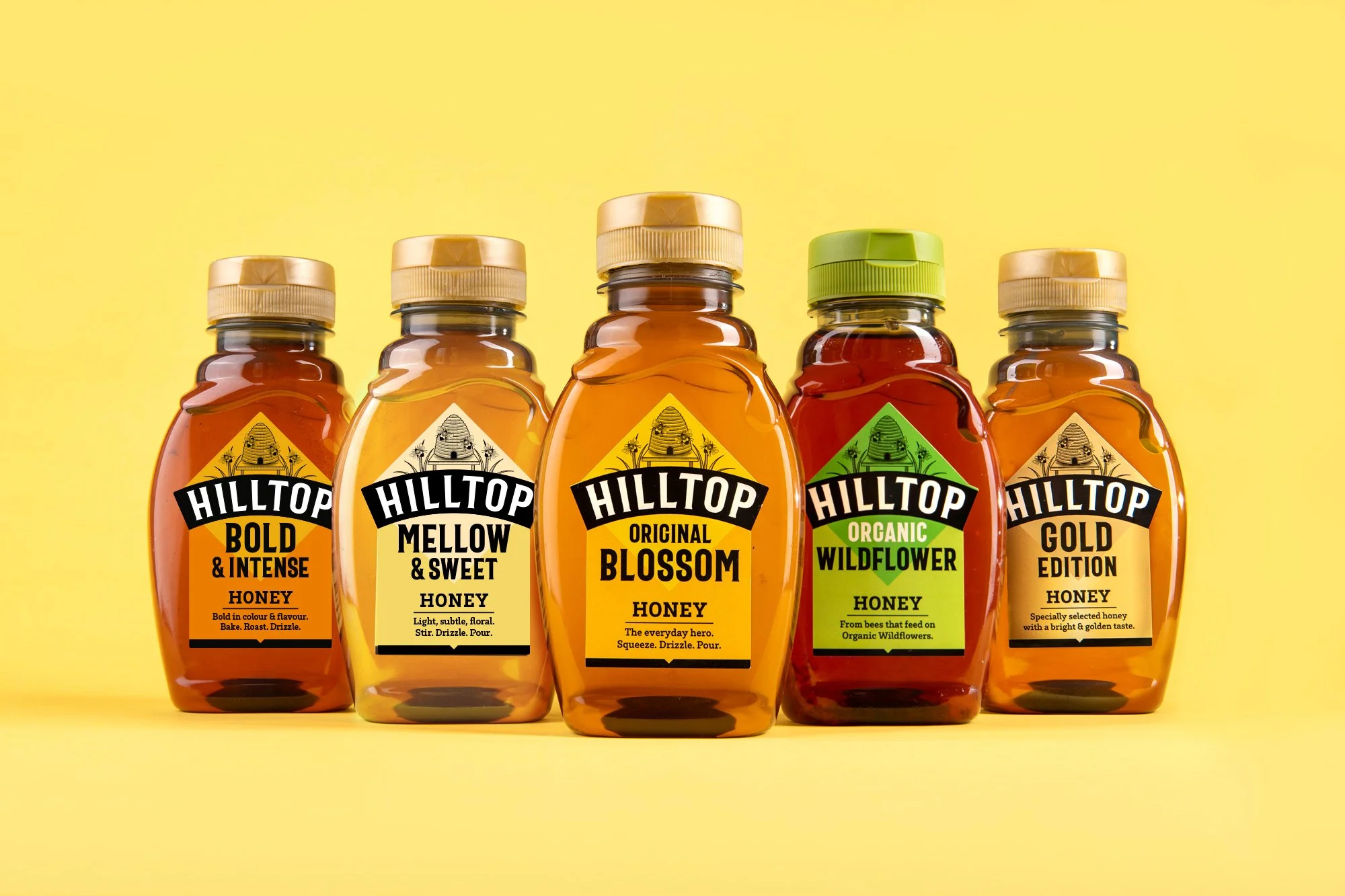 Five bottles of Hilltop honey with different labels: Bold & Intense Honey, Mellow & Sweet Honey, Original Blossom Honey, Organic Wildflower Honey, Gold Edition Honey, set against a yellow background.