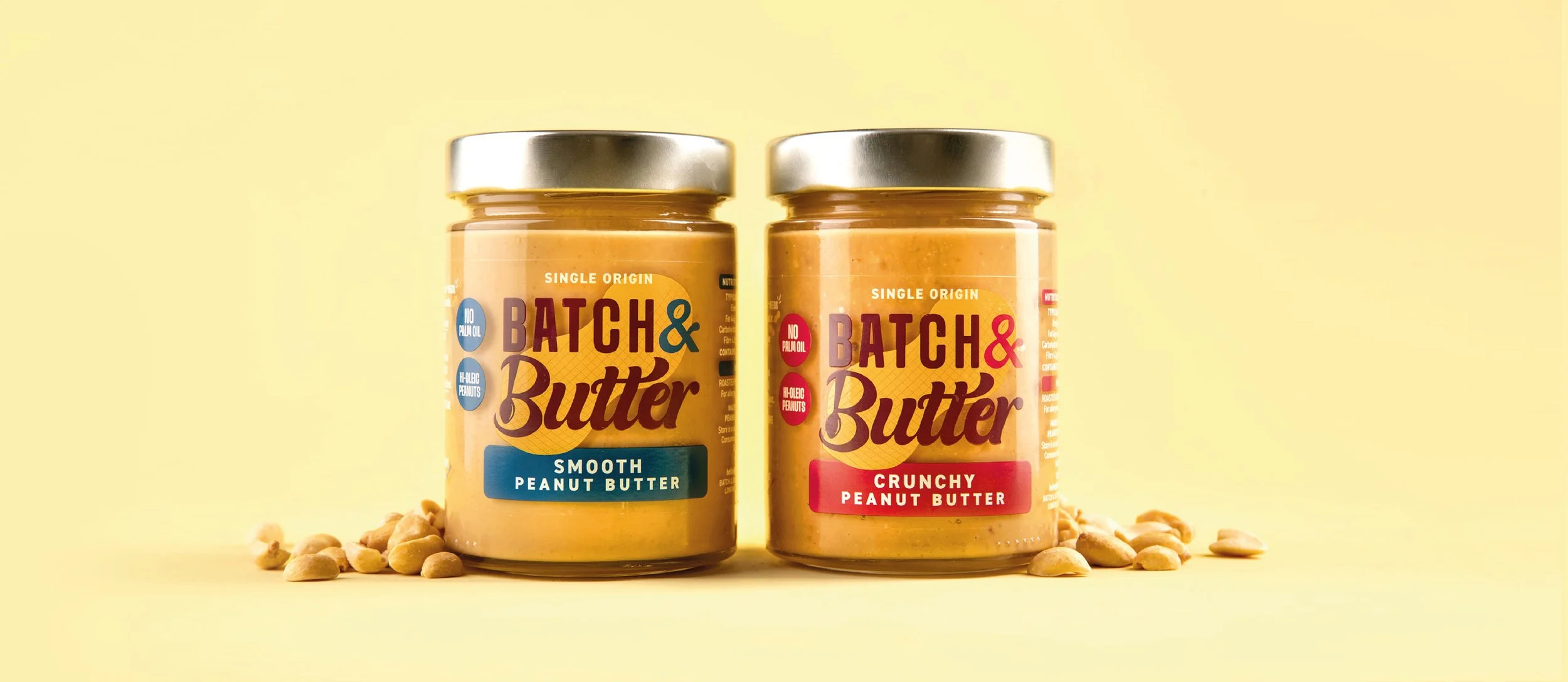 Two jars of Batch & Butter peanut butter, labeled 'Smooth Peanut Butter' and 'Crunchy Peanut Butter,' with scattered peanuts around them, against a yellow background.
