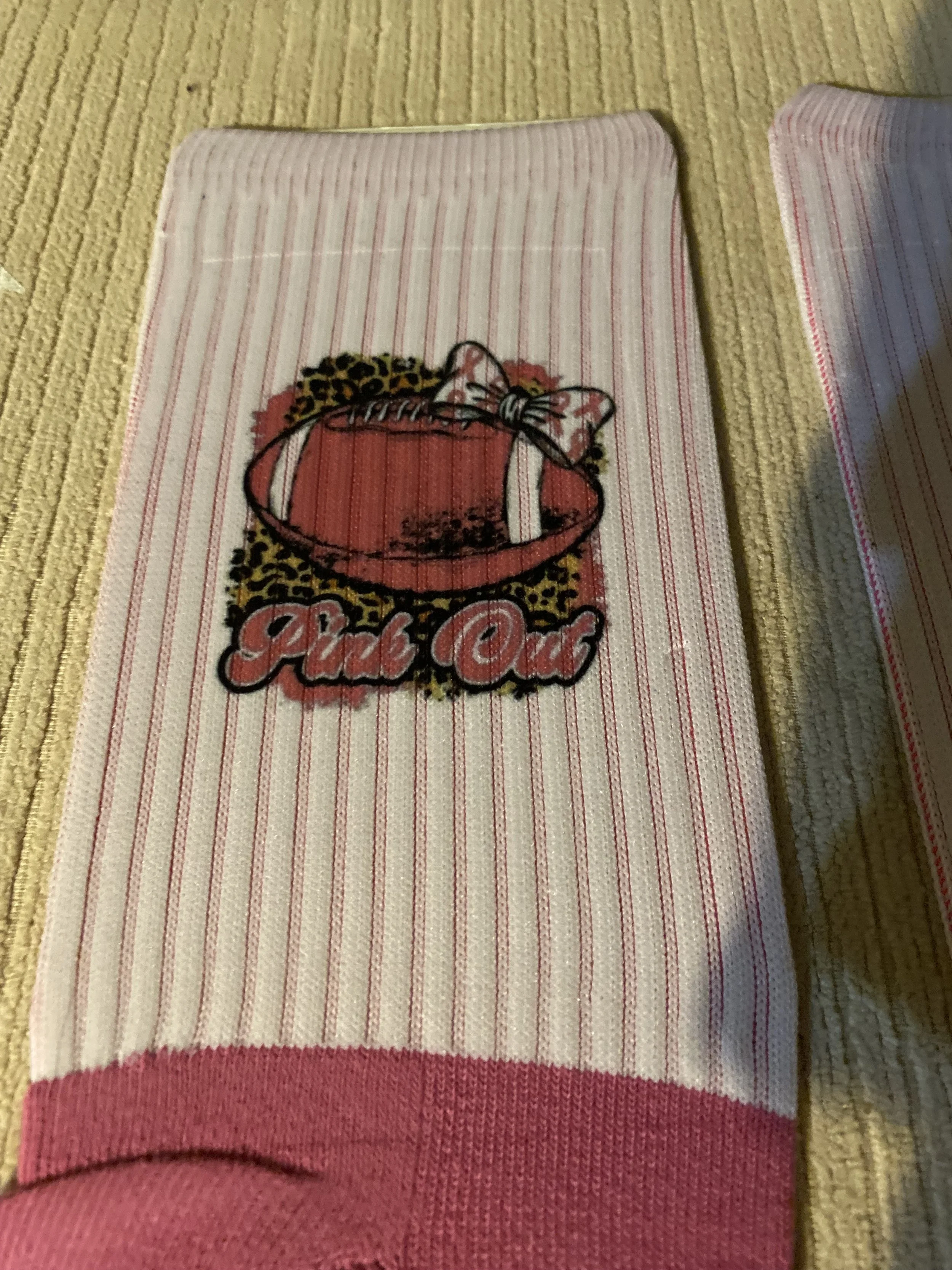 Close-up of a folded white towel with red stripes and a decorative embroidered logo featuring a gift box with a bow, surrounded by the words "Fabulous" and leopard print accents, placed on a woven yellowish rug.