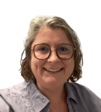 Une femme souriante avec des lunettes, cheveux gris, portant une chemise bleue claire.