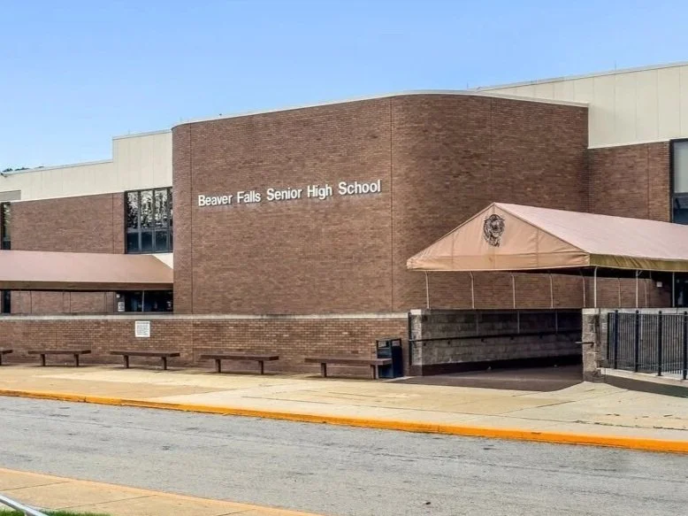 Exterior of Beaver Falls Senior High School with brick walls, a canopy, and a sidewalk in front.