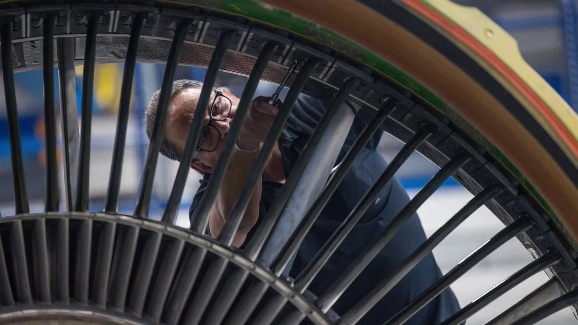 A person working on a machine or industrial equipment, seen through metal bars or grill within an industrial or workshop setting.