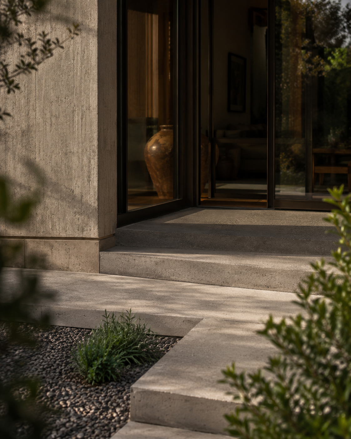 Modern house exterior with glass sliding doors, concrete steps, and garden plants.