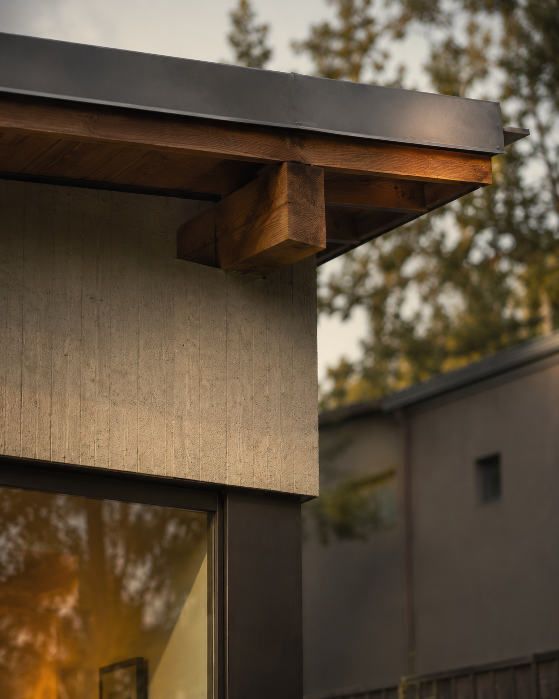 Close-up of modern house exterior corner showing wood and concrete siding with roof overhang and a window.