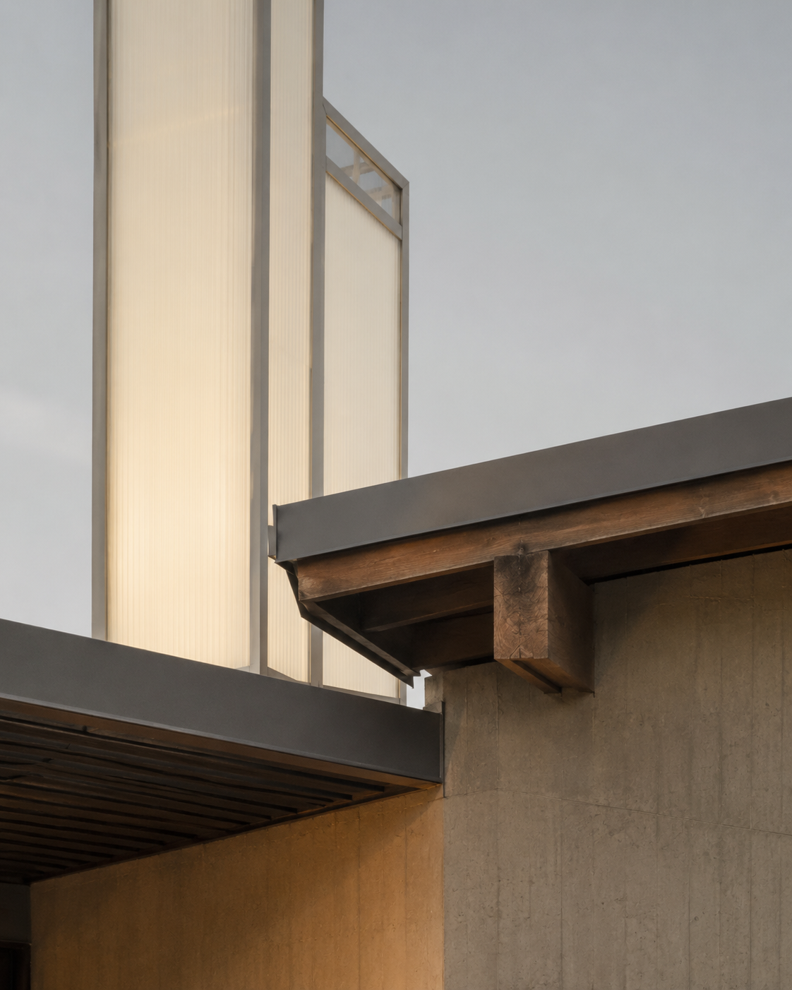 Close-up of the corner of a modern building featuring beige translucent panels, a wooden beam, and metal framing.