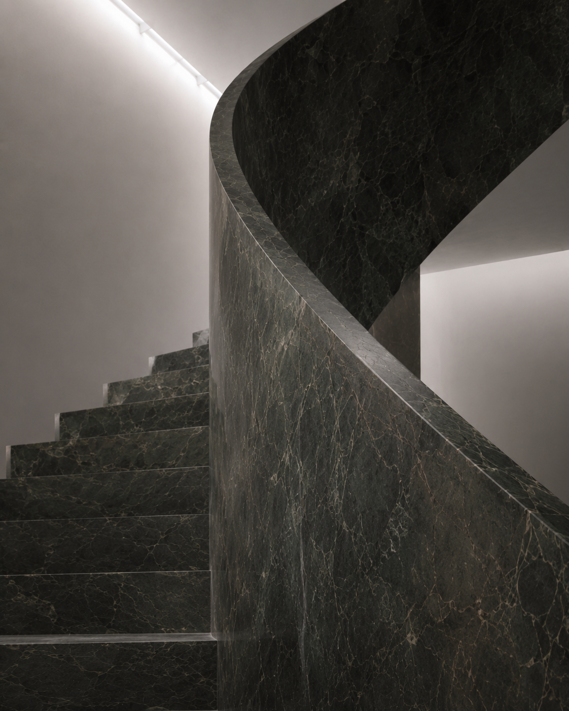 A modern staircase made of dark green marble with white veining, featuring a curved design and minimalistic white walls in the background.