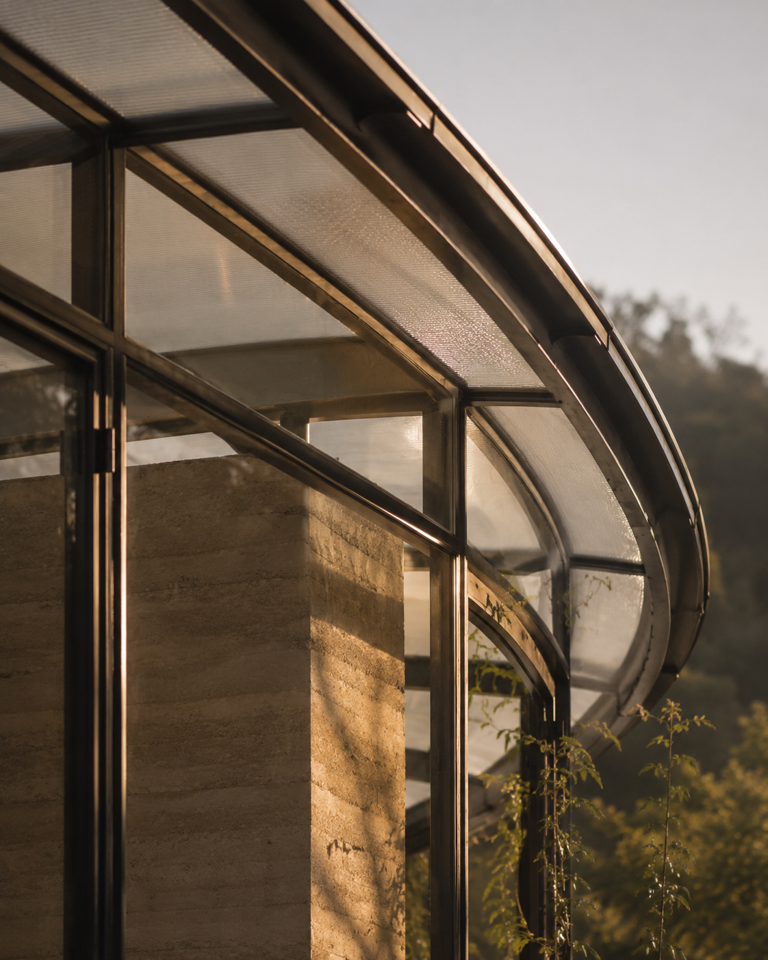 Close-up of a modern building with glass windows and curved metal framing, with sunlight reflecting off the surfaces.
