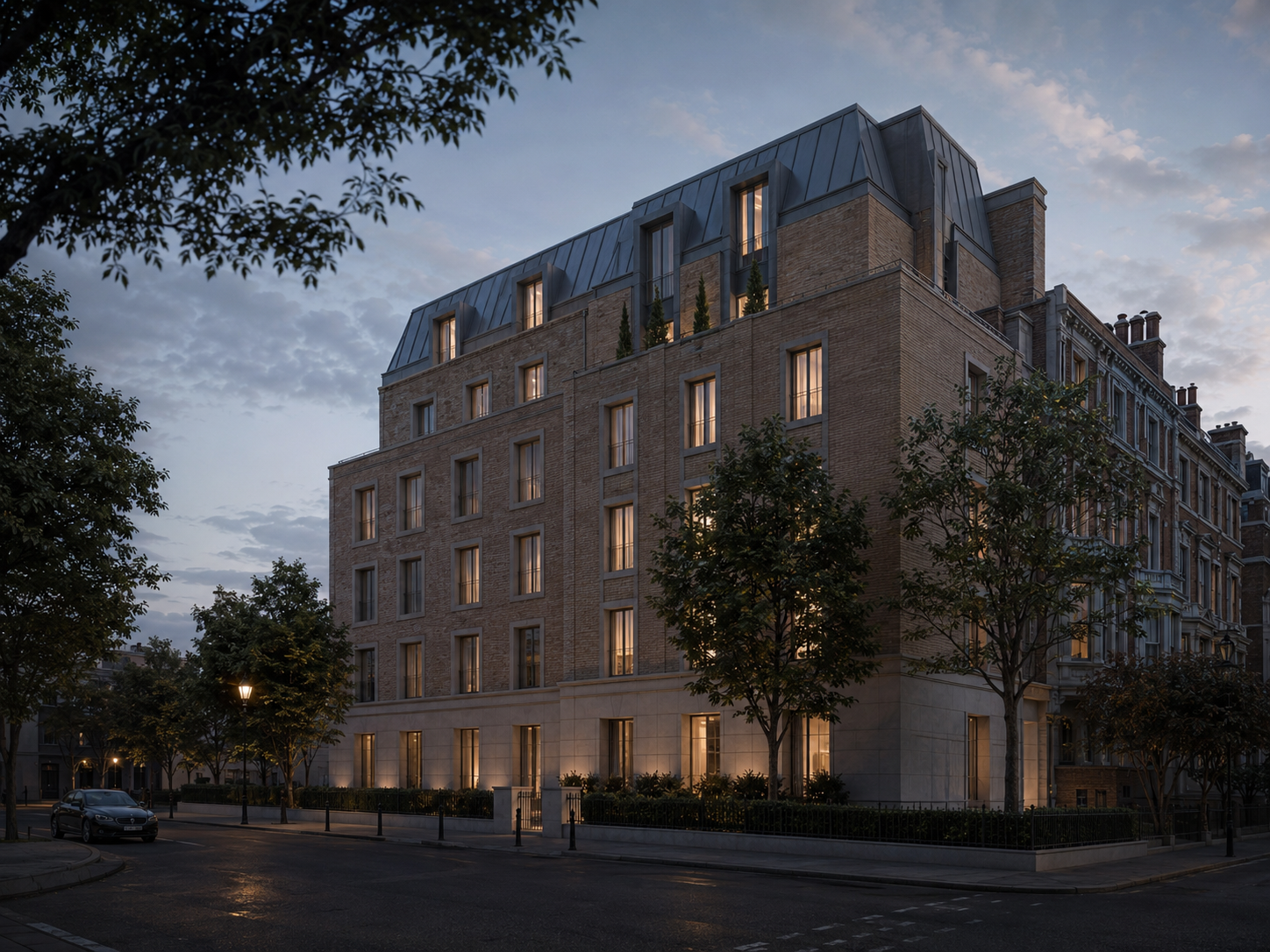 Large multi-story residential building with lit windows at dusk, trees lining the street in front, and a car parked on the road.