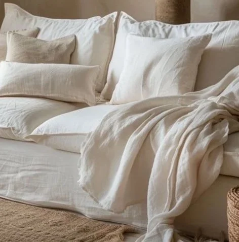 Cama de colores claros con mantas y almohadas blancas y beige.