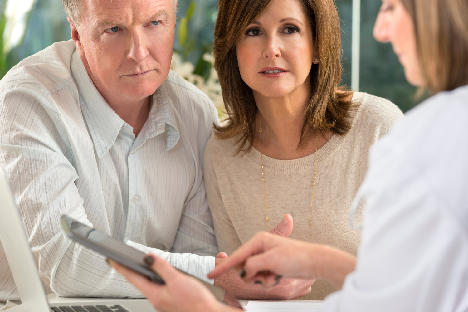 Two middle-aged adults, a man and a woman, talking to a healthcare professional in a consultation room.