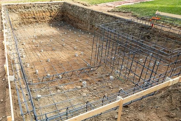 Construction site with steel rebar framework and wooden formwork for a building foundation.
