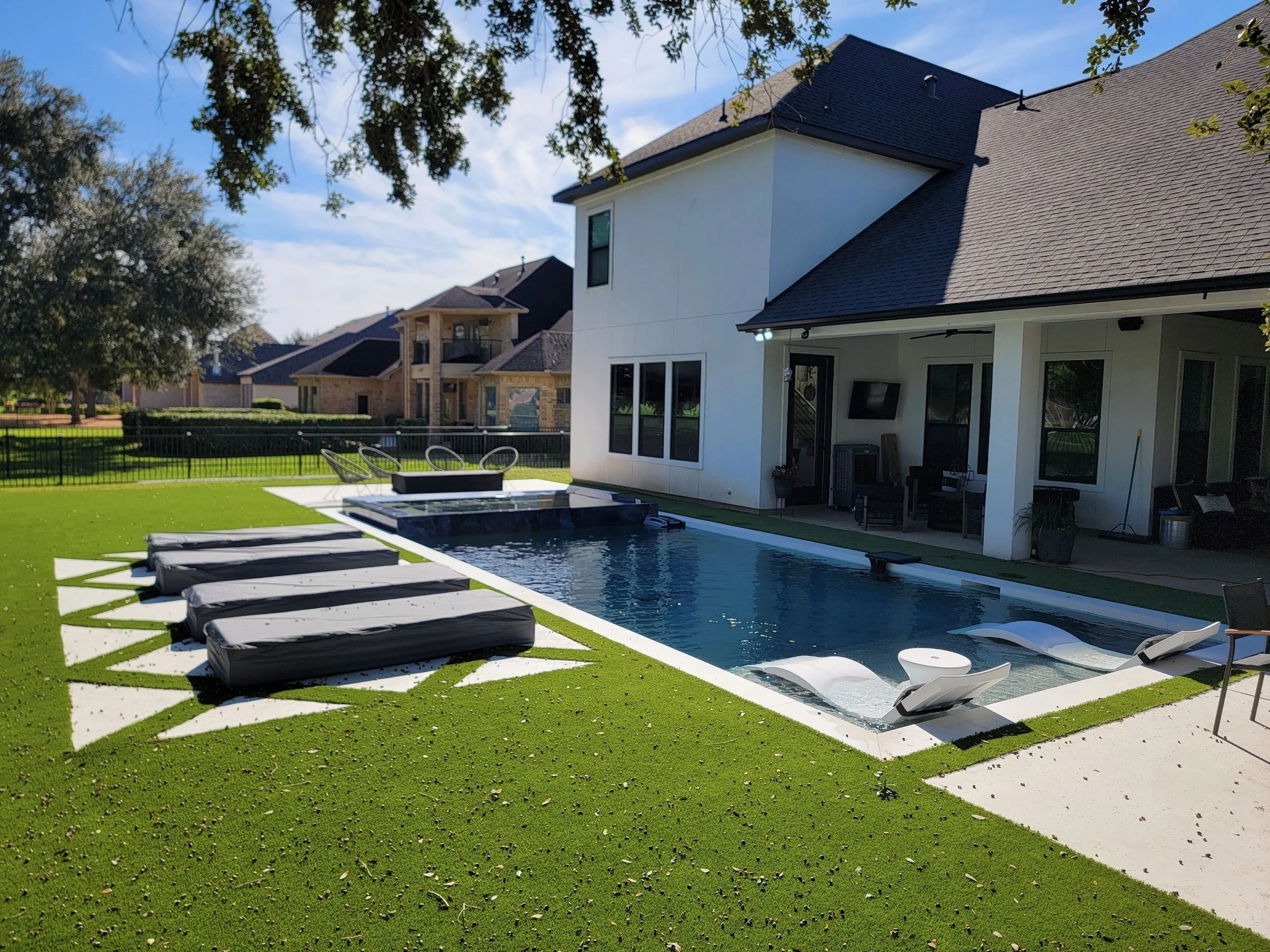 Backyard with a swimming pool, multiple lounge chairs, and a white house with patio.