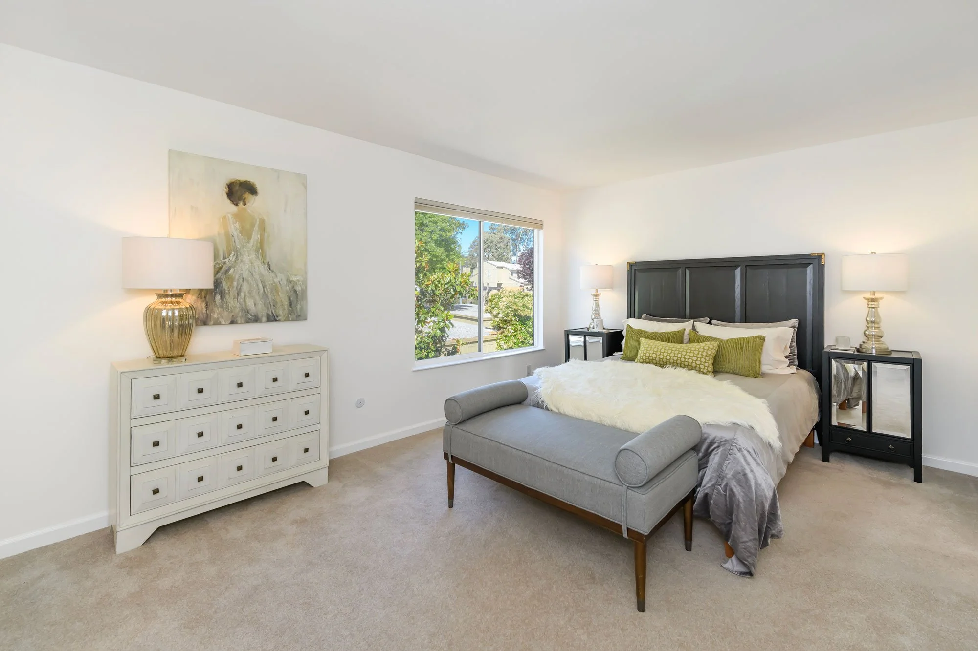 A bright bedroom with a bed, nightstands, and lamps, featuring white walls, a window with greenery outside, and modern decor.