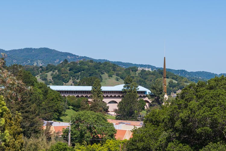 Landscape view of a city with a building featuring a blue roof, surrounded by green trees and hills in the background.