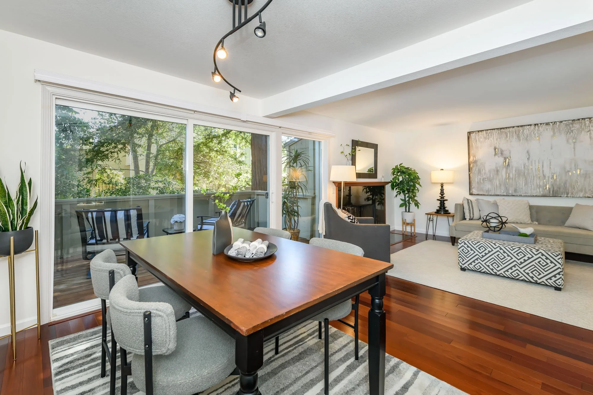 Living room and dining area with large sliding glass door leading to a balcony, wooden flooring, contemporary furniture, plants, and artwork.