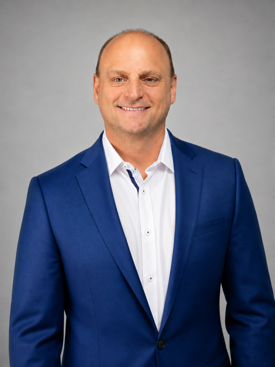 A portrait of Ty Terrell, your mediation expert, a middle-aged man with a bald head, blue eyes, and a friendly smile, dressed in a white shirt and blue blazer against a grey background .