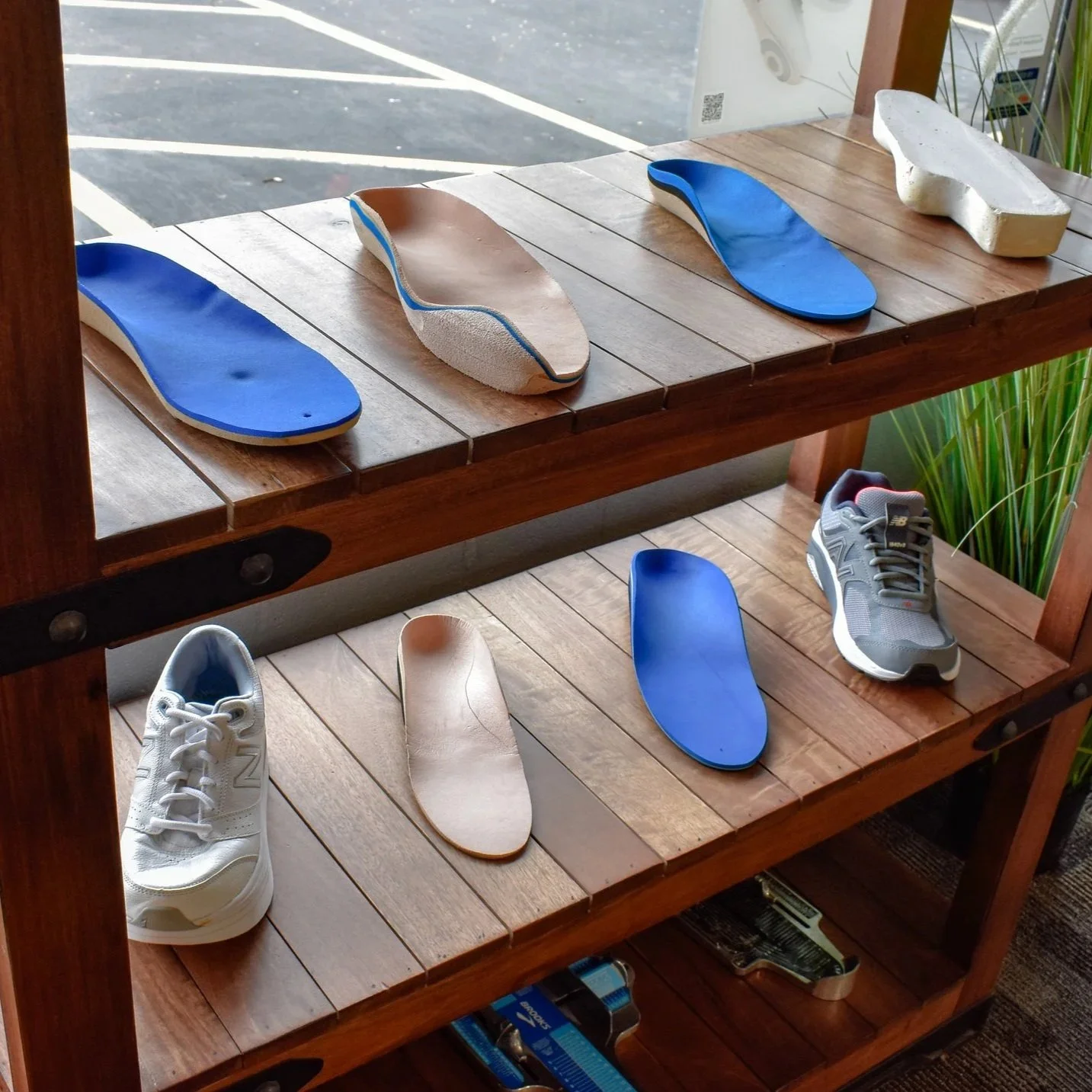 Multiple shoe insoles and two sneakers displayed on a wooden shelf inside a store.