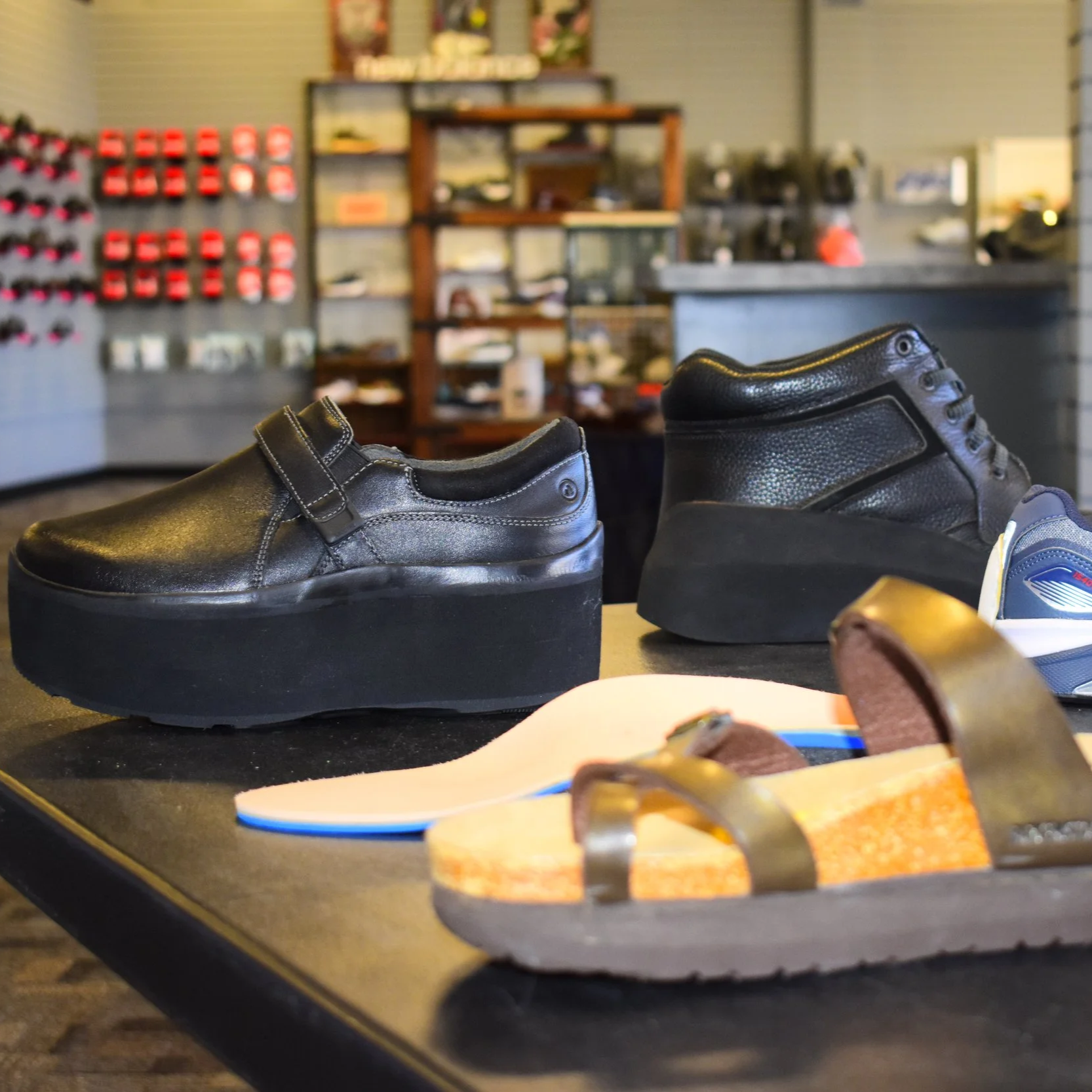 Display of various shoes including black platform shoes,Platform sneakers, and sandals inside a store with shelves and wall displays in the background.