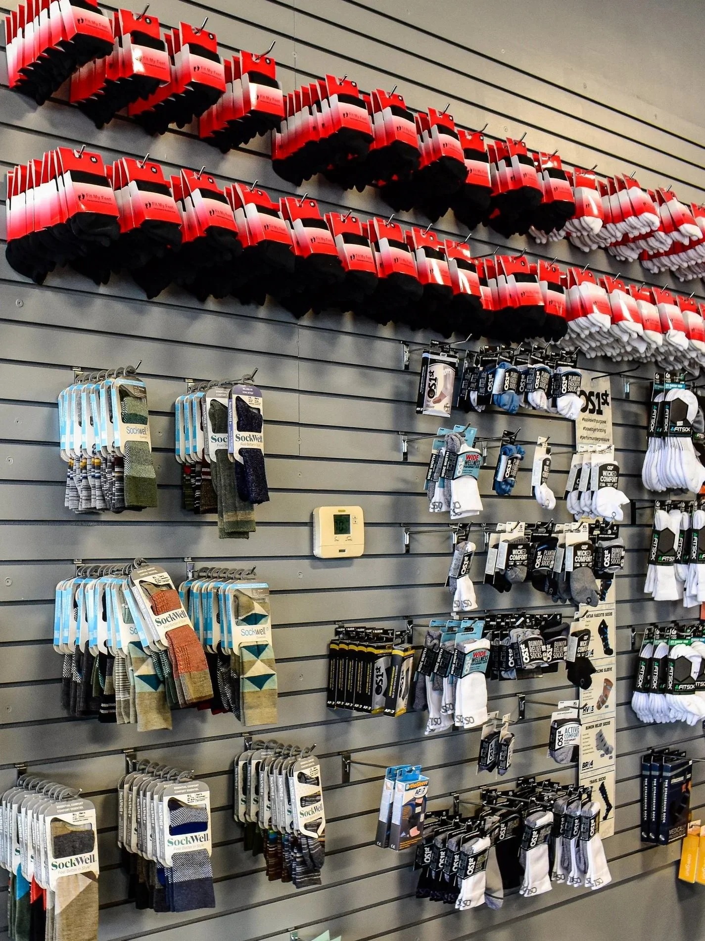 Display of neatly arranged men's socks on a slatwall in a retail store, featuring various colors and styles, including black, white, gray, and patterned options.