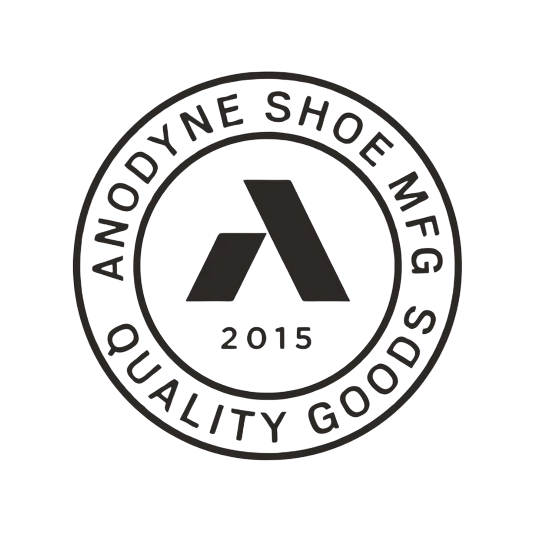 A black and white circular badge with the Omega logo in the center, the year 2015, and the phrase 'Anodyne Shoe' on top and 'Quality Goods' on the bottom.