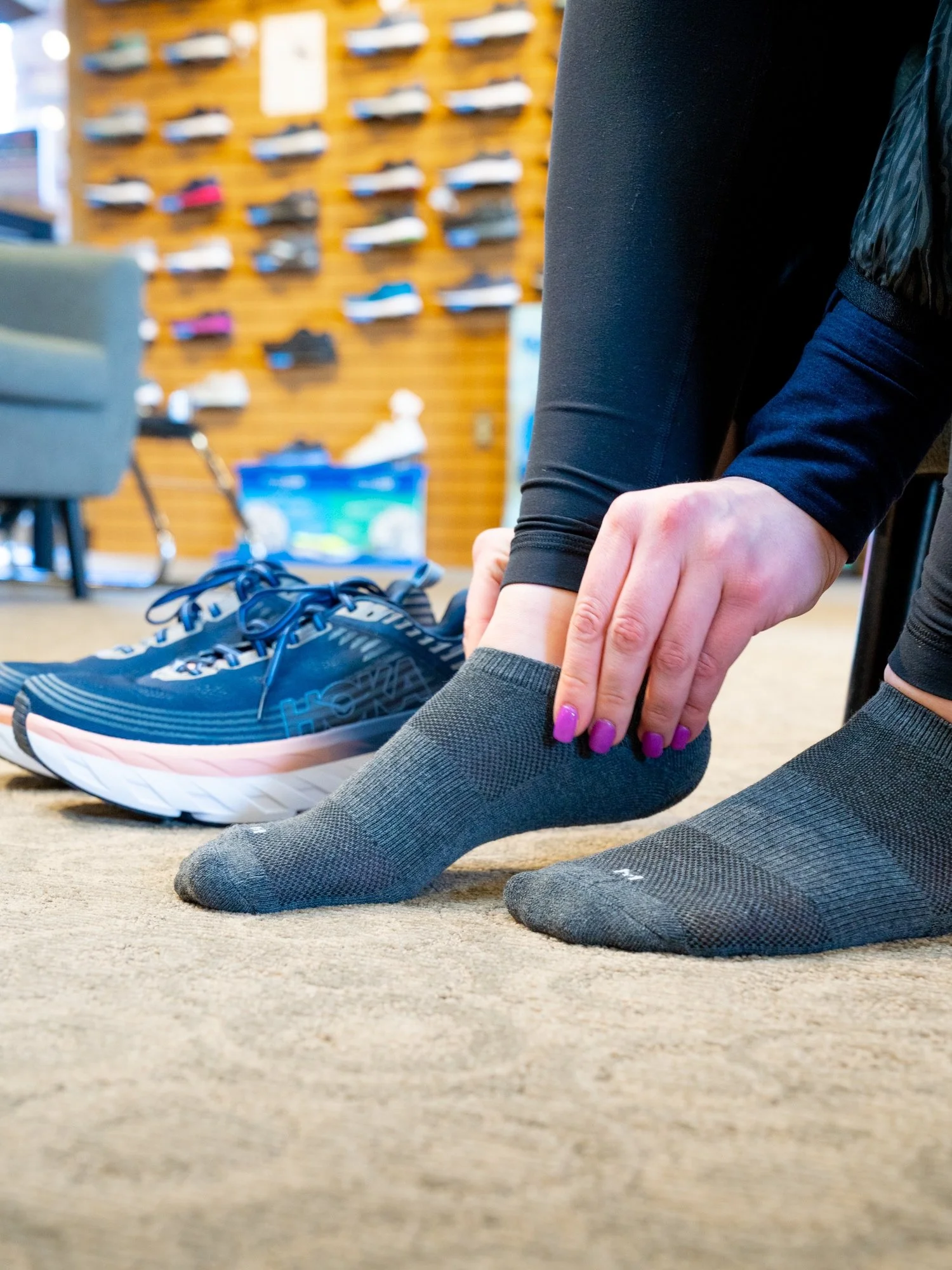 Person adjusting a grey sock while bending over on a carpeted floor at Fit My Feet Sioux Falls, SD.