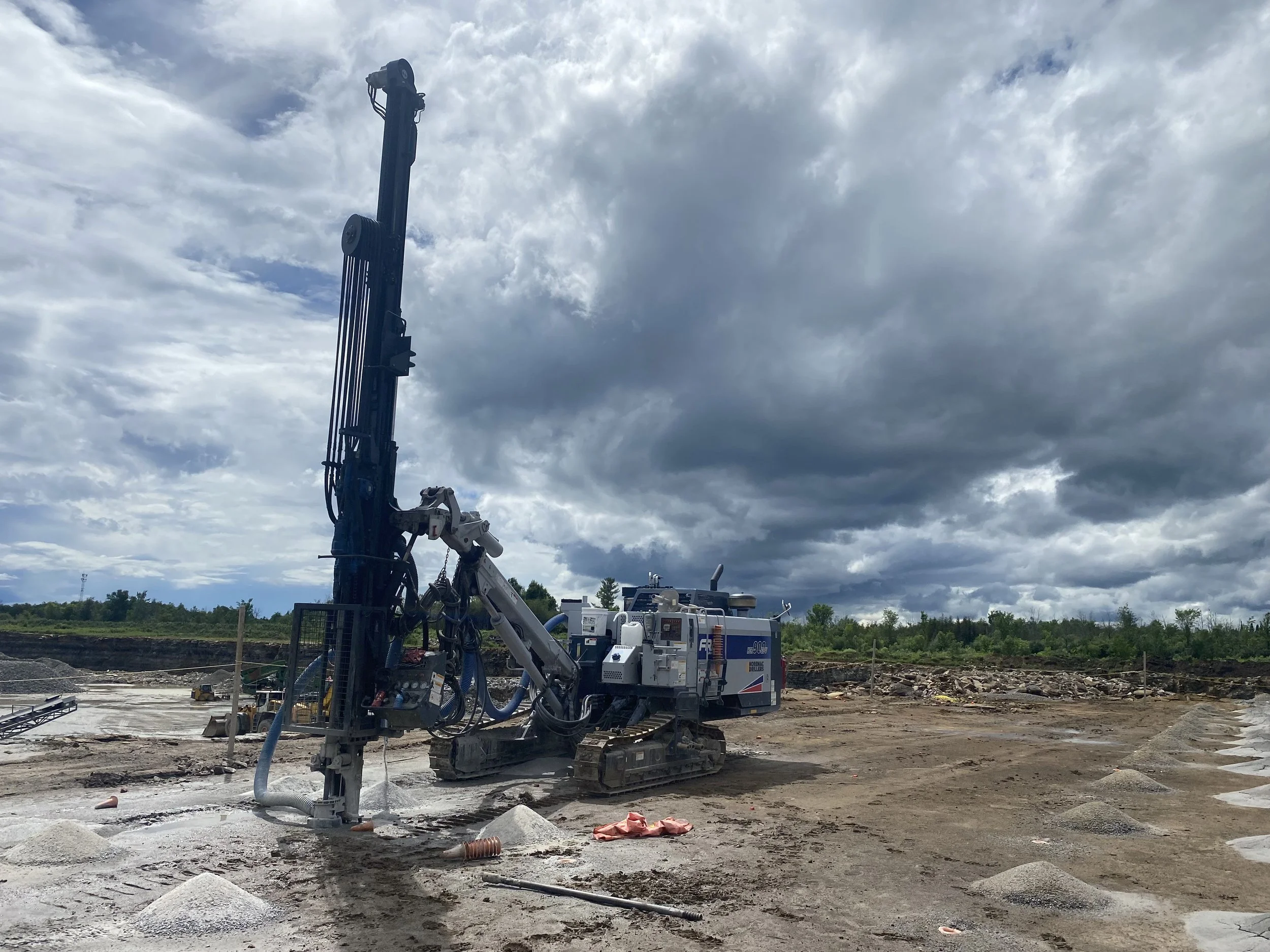 Construction site with drilling machinery, cloudy sky, and ongoing earthwork.