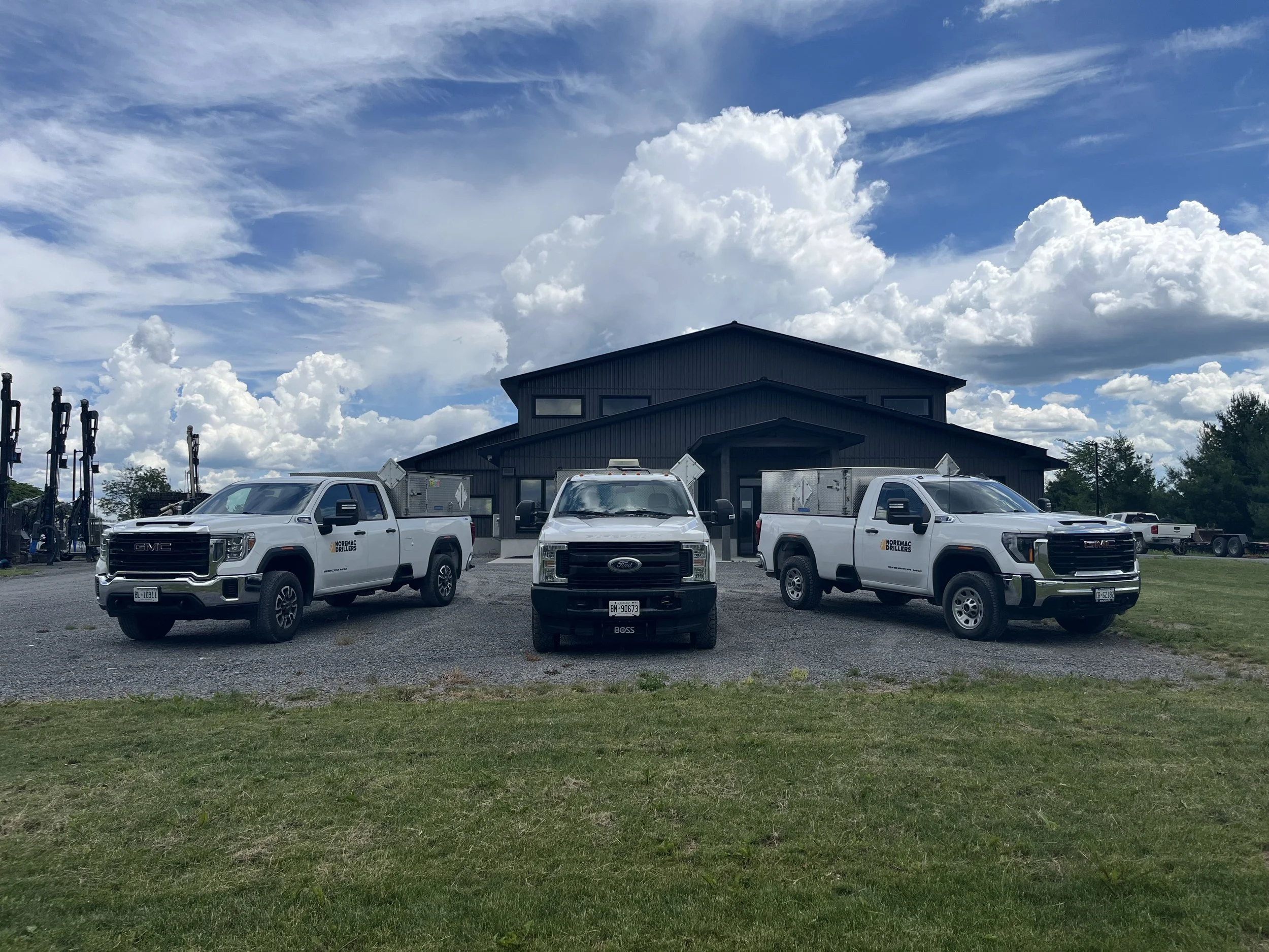 A parking lot with several white trucks parked in front of a dark gray building under a partly cloudy sky.