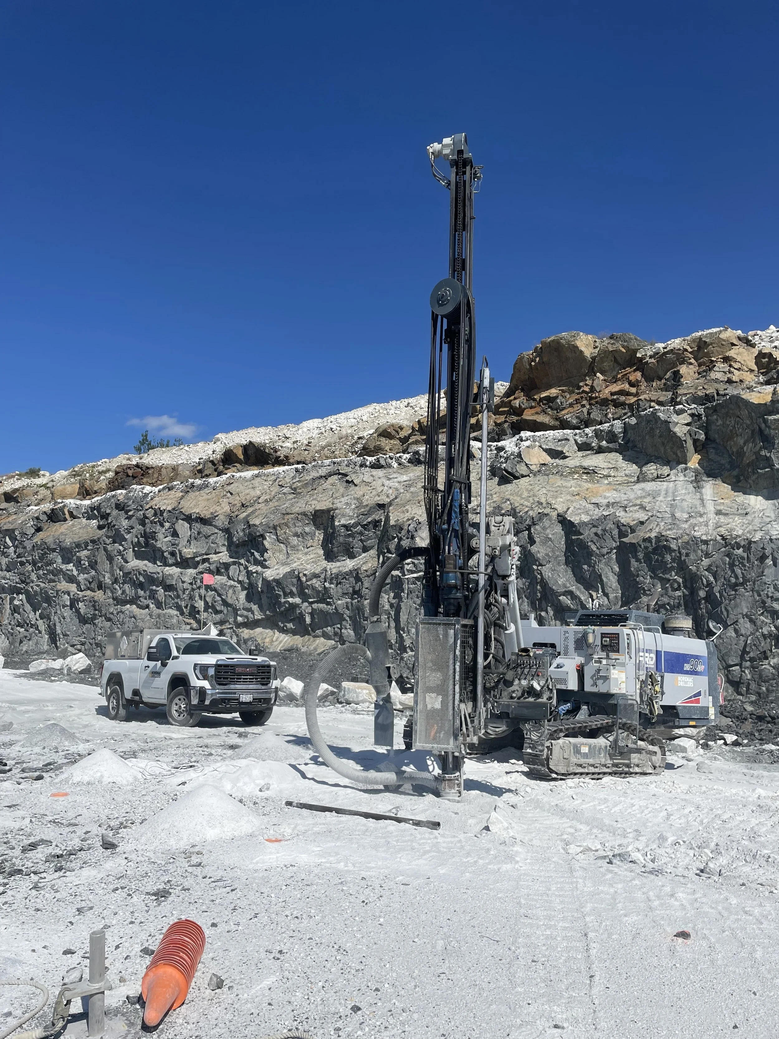 Construction site with heavy machinery, a pickup truck, and rocky terrain under a clear blue sky.