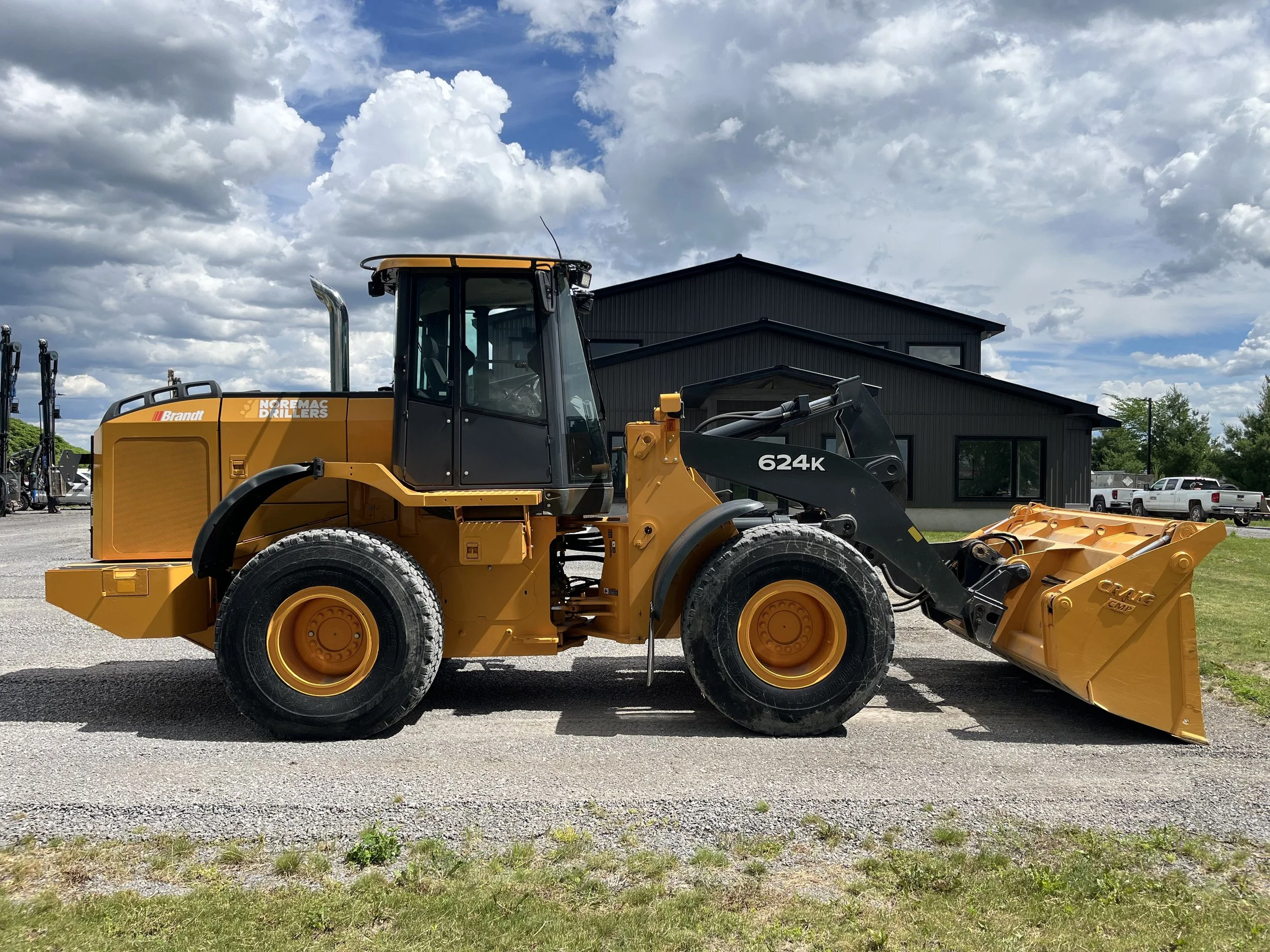 Yellow construction front loader with black cabin and large tires parked on gravel in front of a modern black building under cloudy sky.