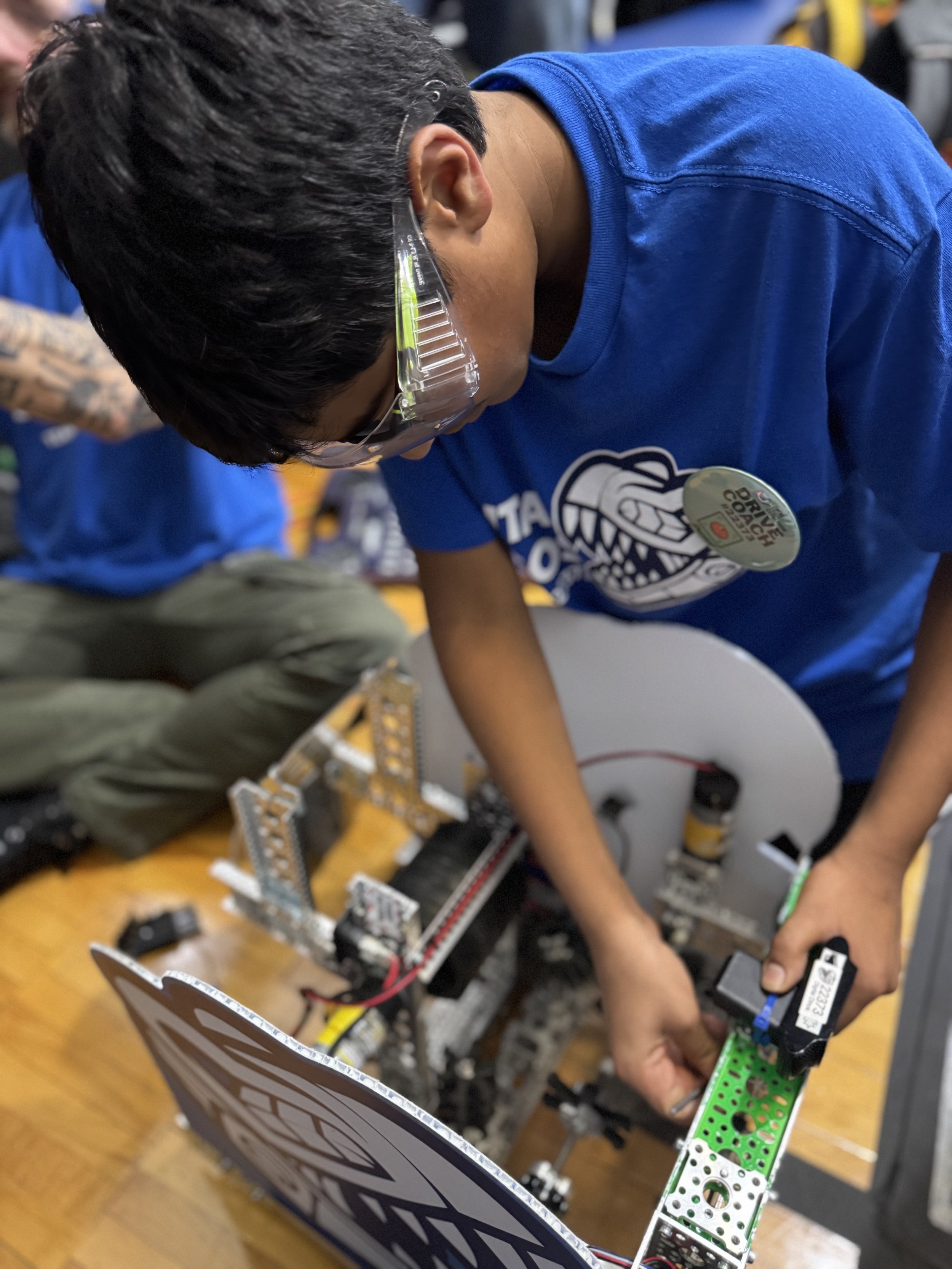 A person wearing safety glasses working on a robotics project with various mechanical and electronic components on a table.