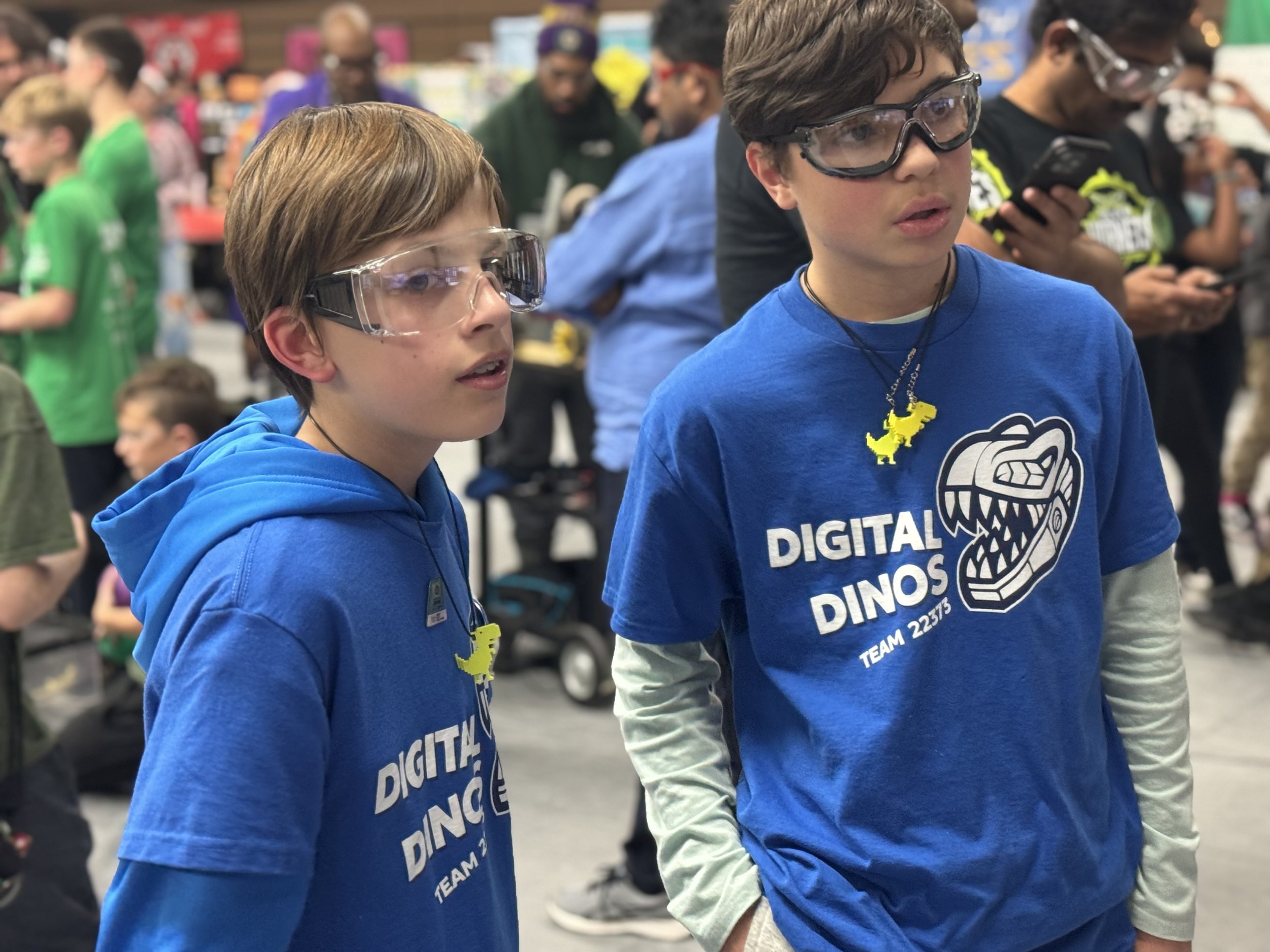 Two boys wearing glasses and blue team shirts at a crowded event.