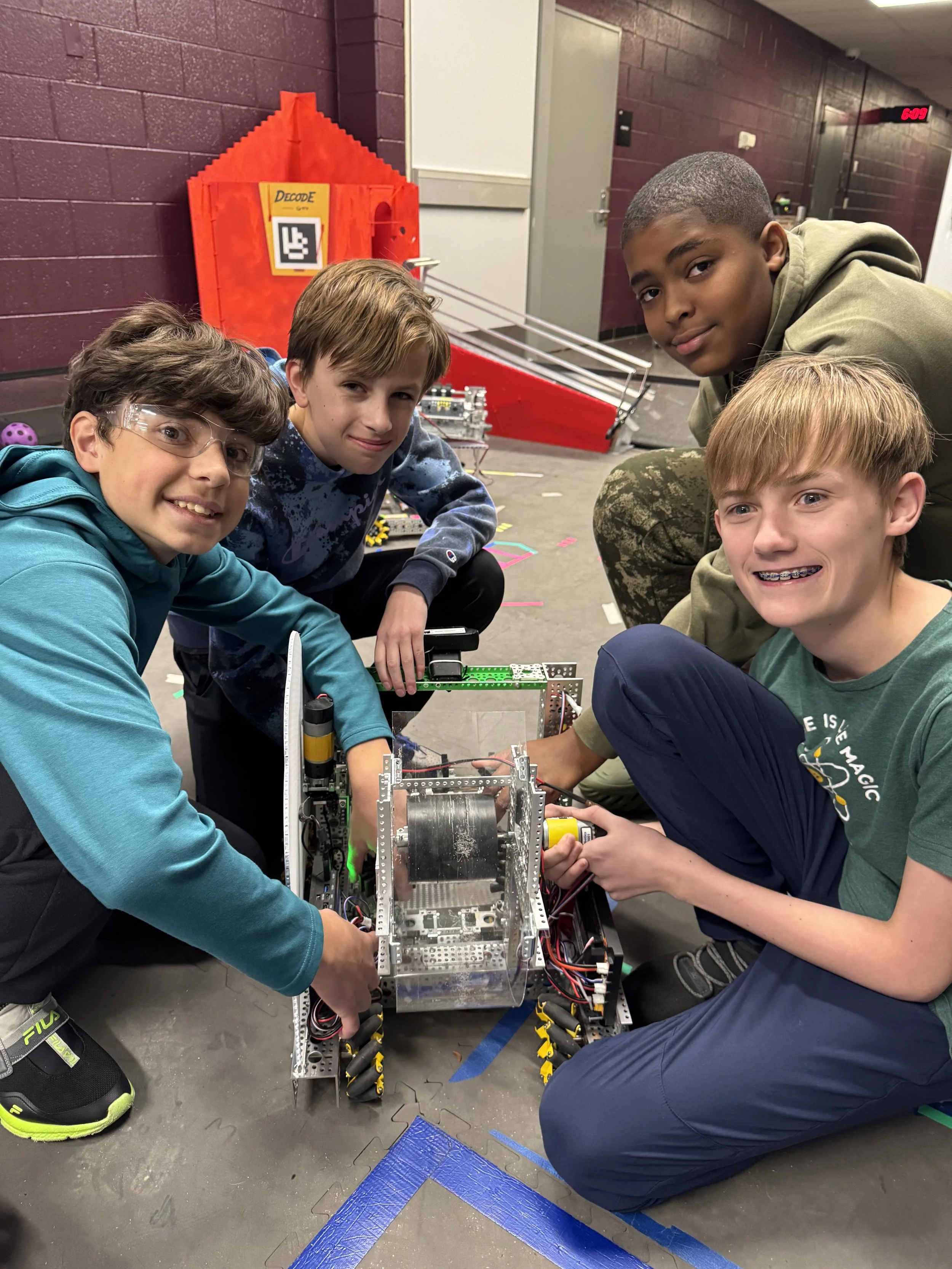 Four boys working together on a robot in a school hallway.