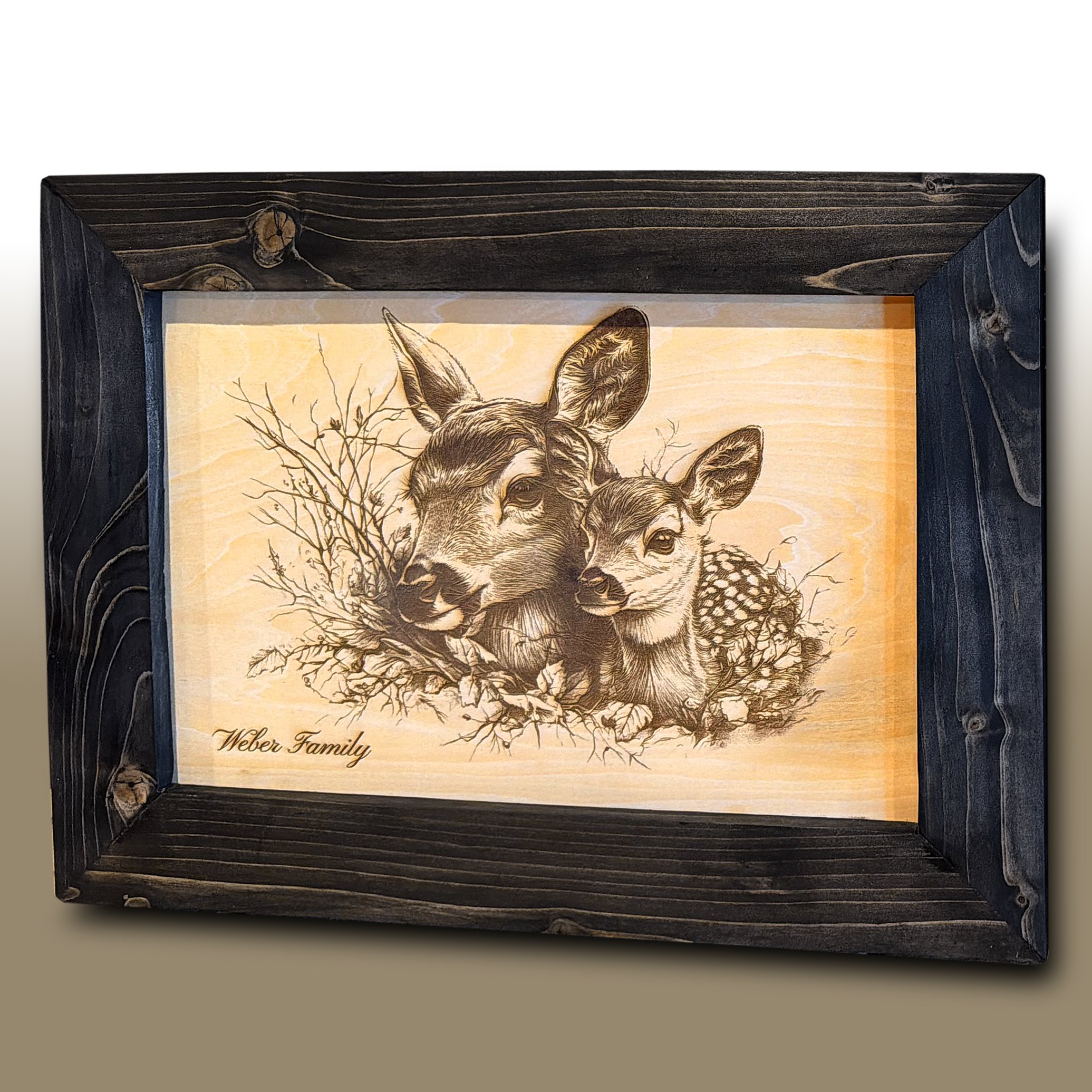 Framed artwork of a deer head with antlers, featuring branches and the words 'Weber Family' at the bottom, encased in a black wood frame with visible knots.