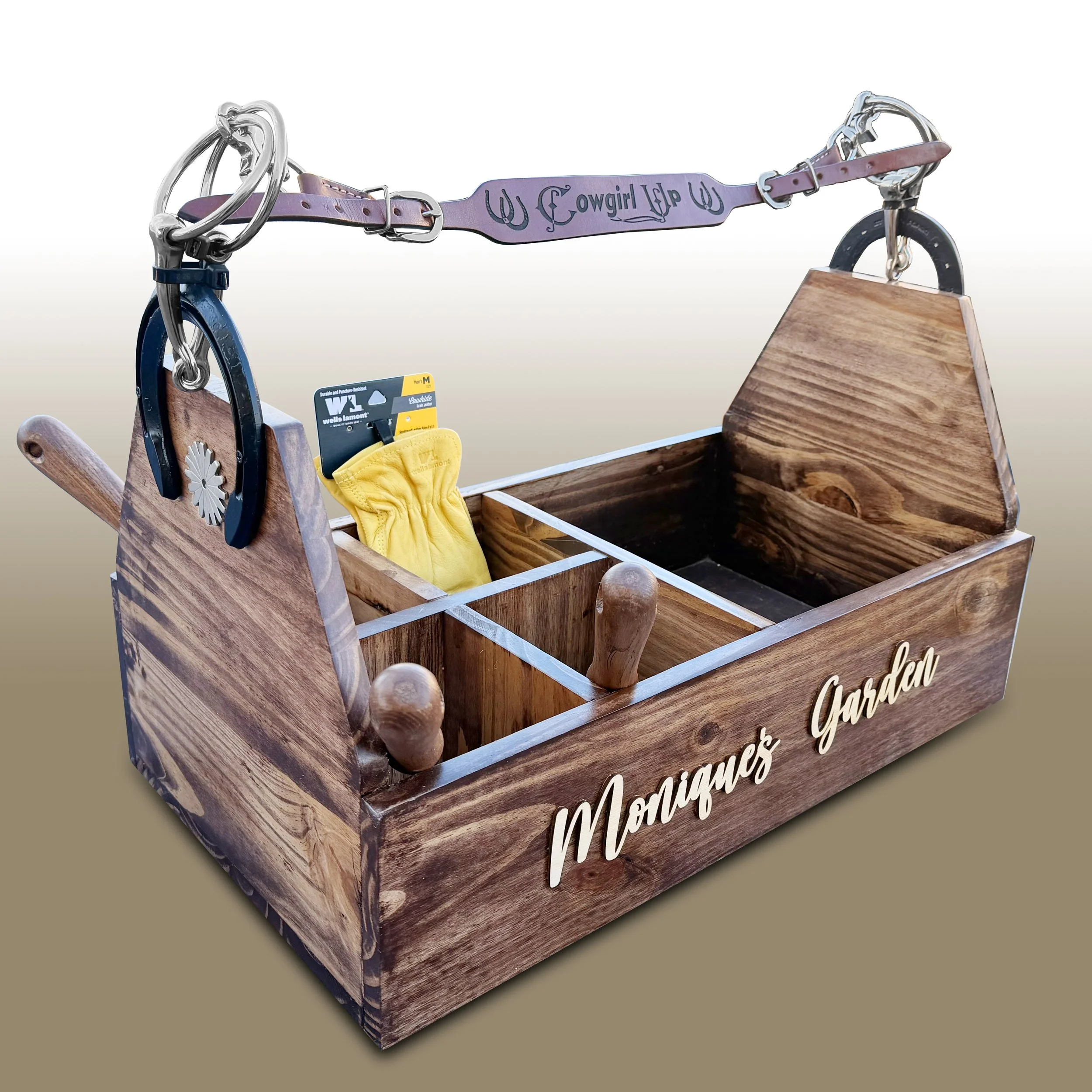 Wooden horse box with a purple strap labeled 'Cowgirl Up' holding a yellow cloth, featuring a wooden stand on top, with part of a decorative sign reading 'Marques Garden' visible.