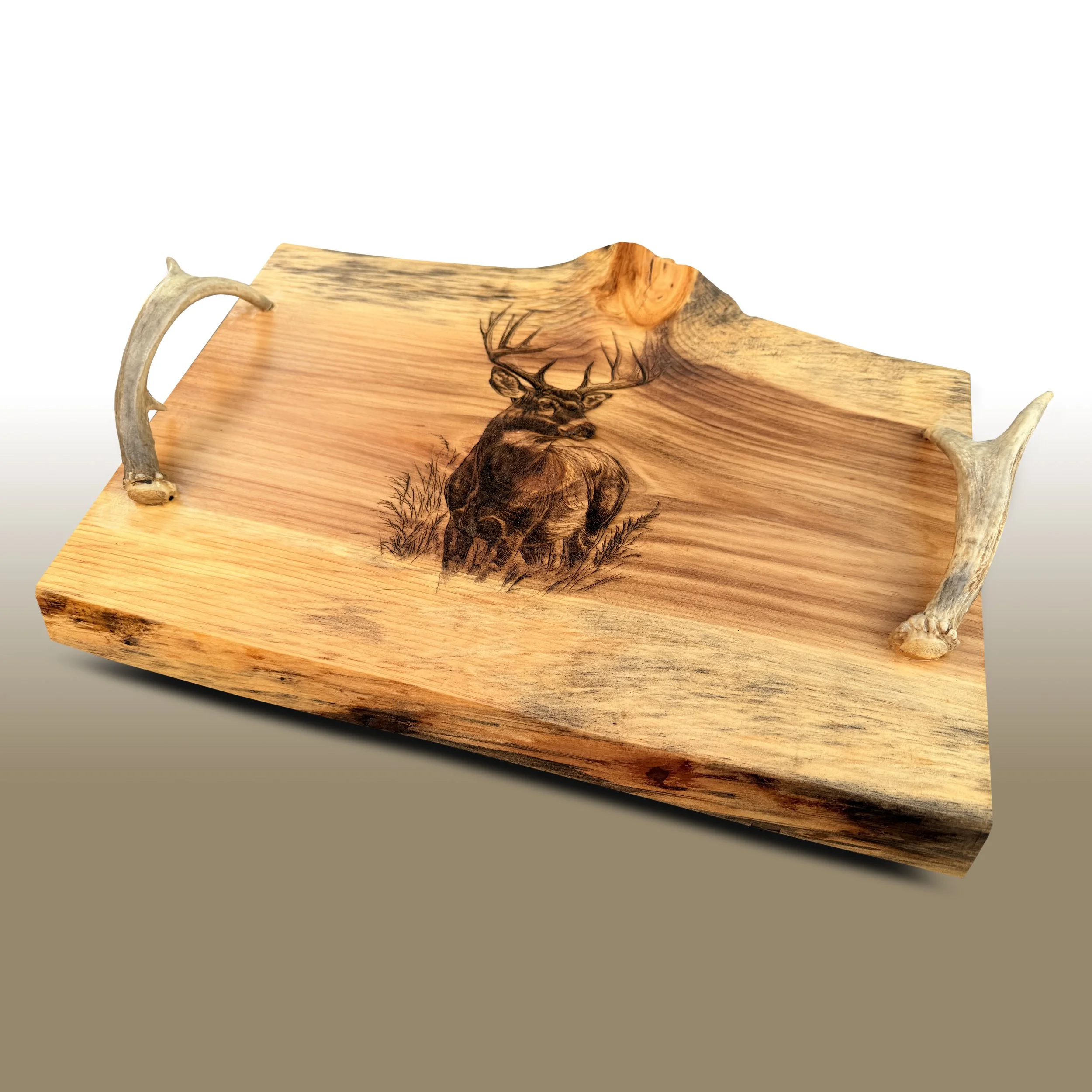 A wooden cutting board with a engraved image of a deer and antlers, and some antlers resting on the board's edges.