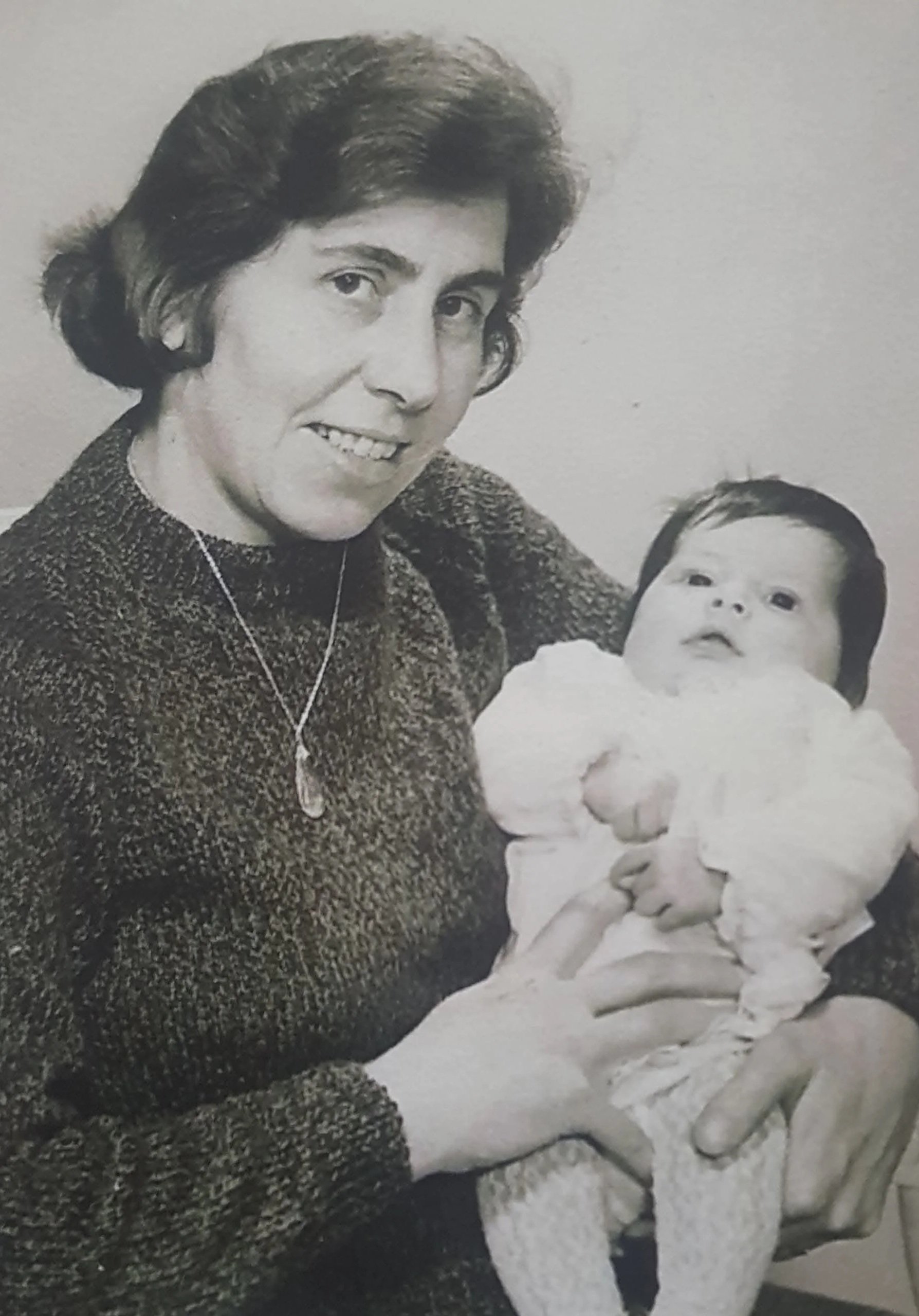 Black and white photo of a woman holding a baby wrapped in a blanket, both looking at the camera.