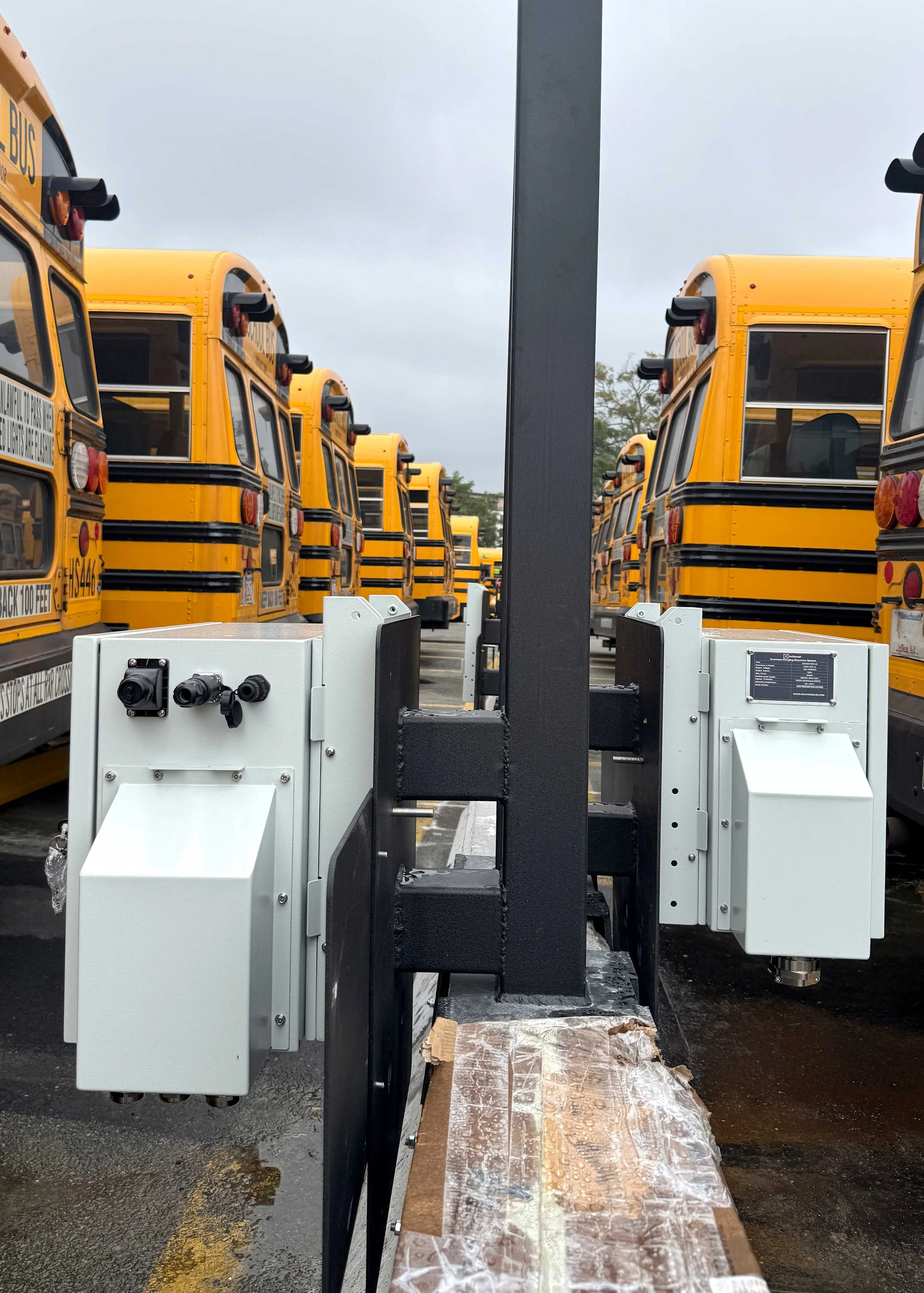 A row of yellow school buses parked outdoors on a cloudy day, with electric vehicle charging equipment in the foreground.