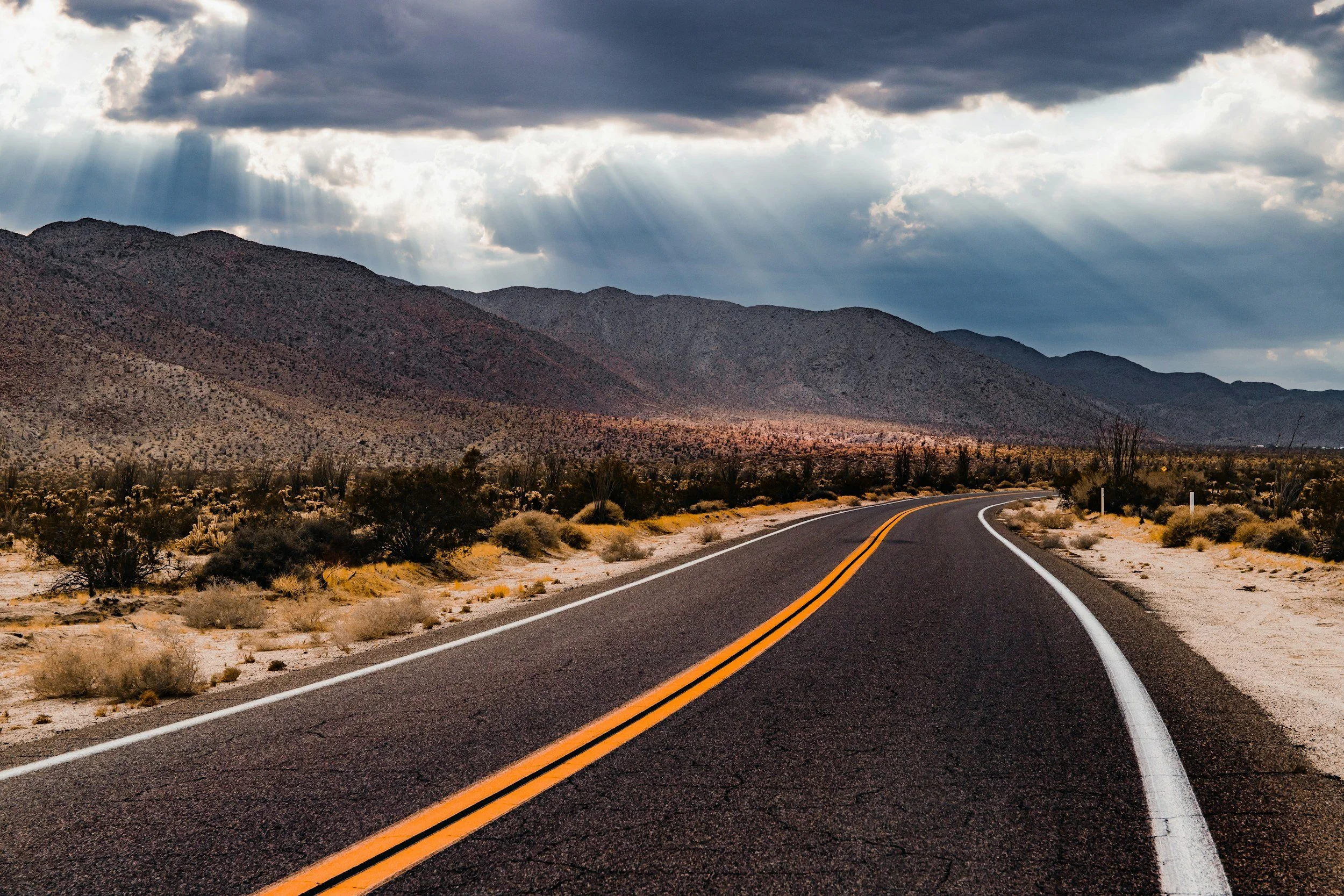 A winding road through a desert landscape with mountains in the background under a cloudy sky with rays of sunlight breaking through. Headline: Engagement Types