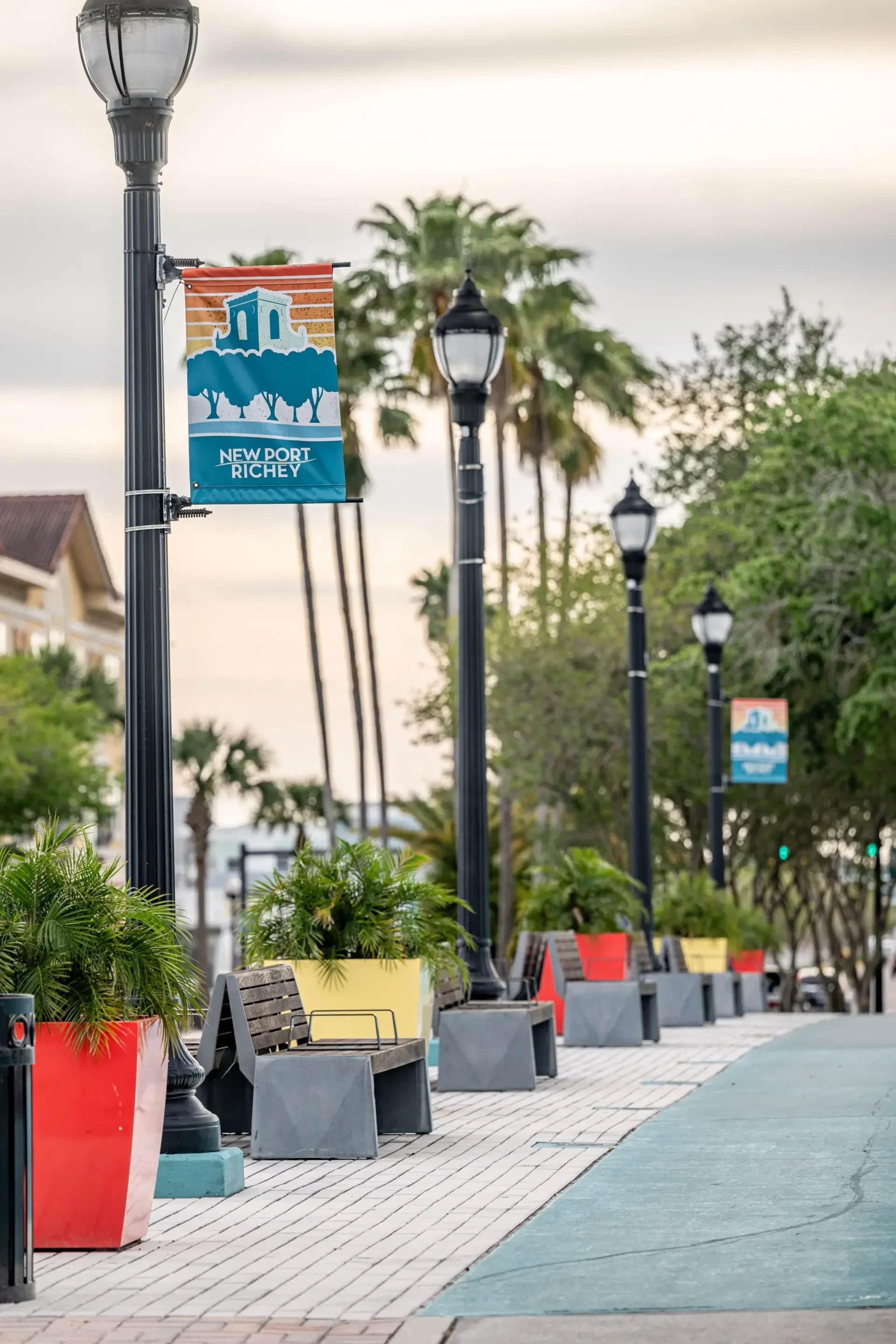 A sidewalk with benches and colorful planters, street lamps, and banners that read 'New Port Richey'.