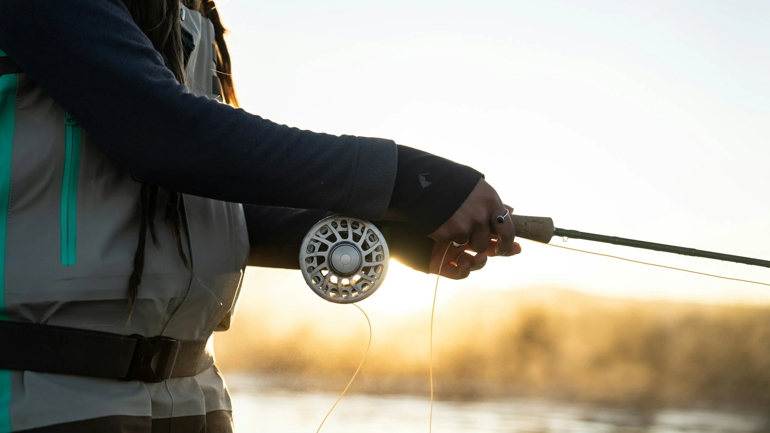 Angler holding a fly rod while fishing at sunset