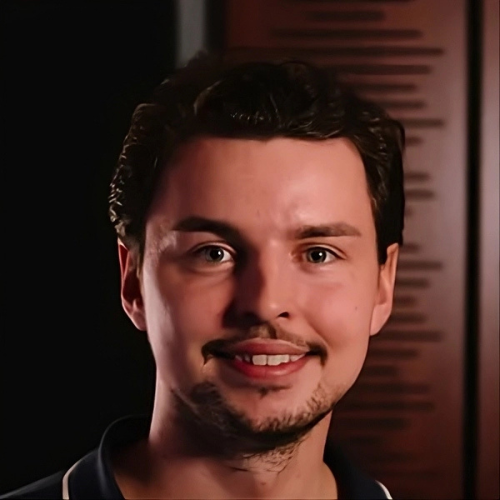 A young man with dark hair and a slight beard smiling at the camera.