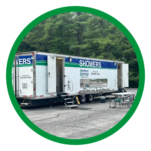 Mobile shower trailer with steps and table, set up outdoors on pavement with trees in the background.