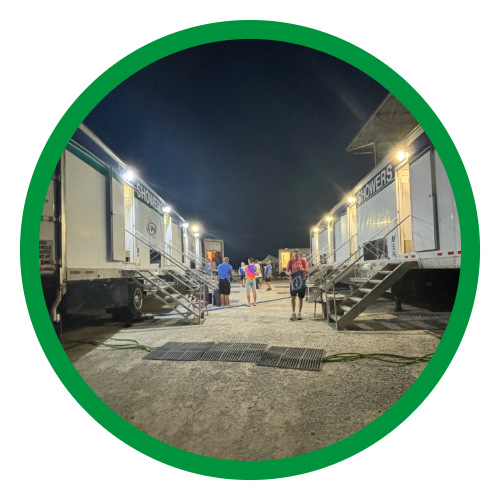People walking between two rows of trailer-style hospitality units at night, under bright lights