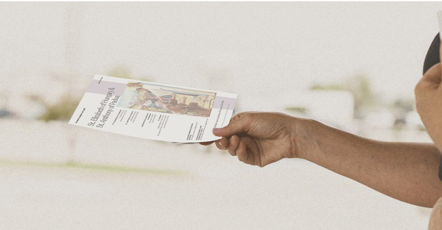 A person holding a flyer about St. Elizabeth of Hungary and St. Anthony of Padua, with an illustration of saints on it.