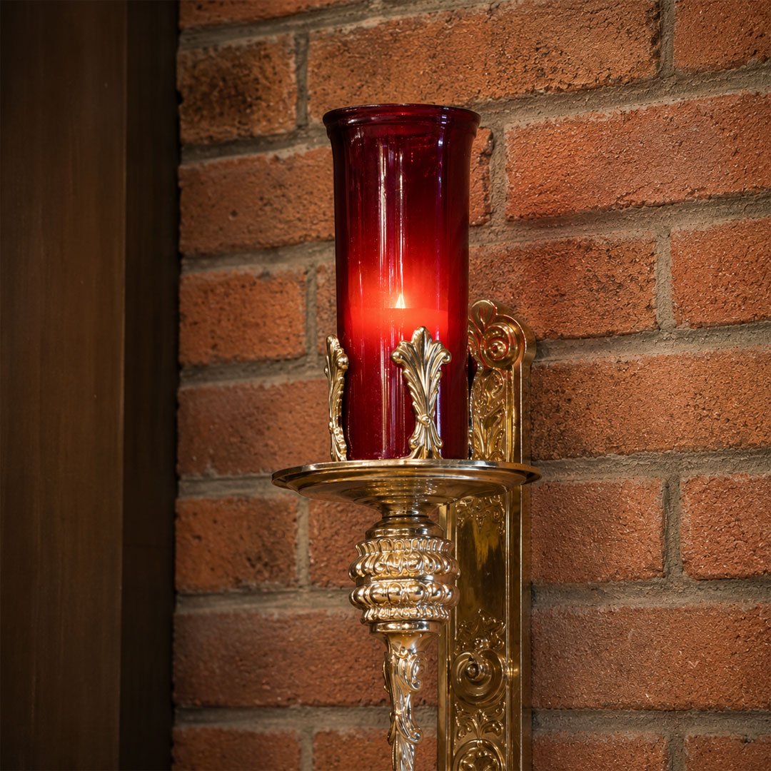 Close-up of an ornate gold wall sconce with a red glass candle holder, mounted on a brick wall.
