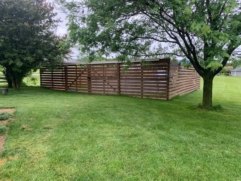 A backyard with a green lawn, trees, and a wooden fence. Iowa City. Stecker Home Services. Home Renovations. Iowa City Contractor. 