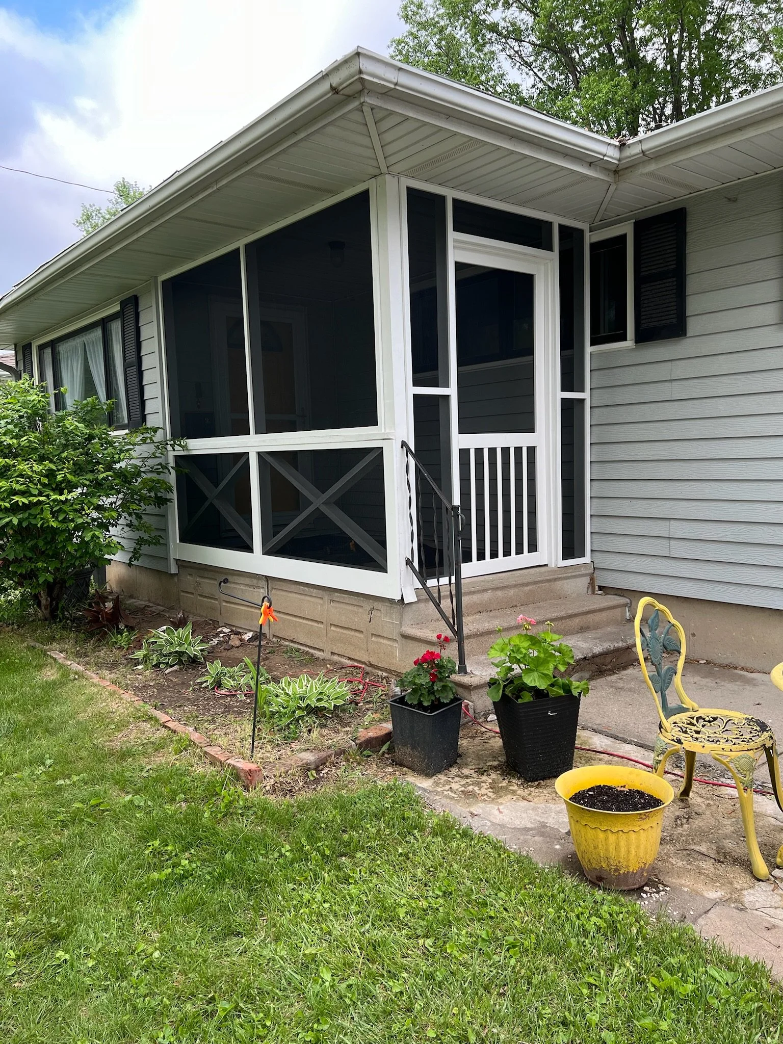 A house with a screened porch, a small garden, potted plants, a yellow decorative chair, and a yellow pot with soil on a concrete patio. Iowa City. Stecker Home Services. Home Renovations. Iowa City Contractor. 